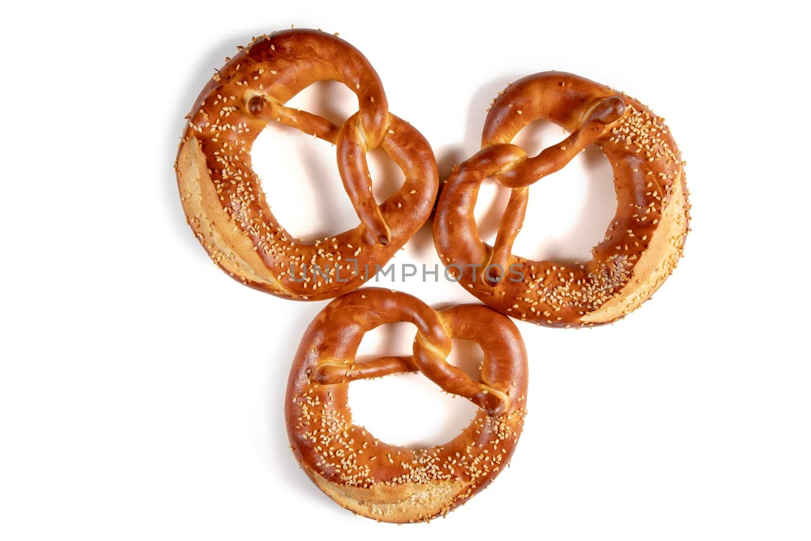 Three golden brown Bavarian pretzel top view with a generous amount of sesame seeds sprinkled over it is shown in this image. The pretzel has a knotted shape and a crispy texture.