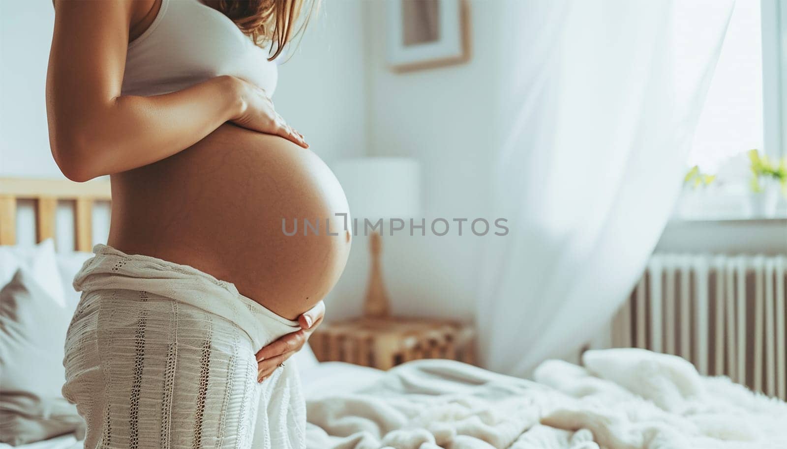 Beautiful pregnant woman holds hands on belly in bedroom at home. Young mother waiting of a baby. Concept of pregnancy, maternity, health care, gynecology, medicine. Close-up, indoors. Stylish boho interior beauty
