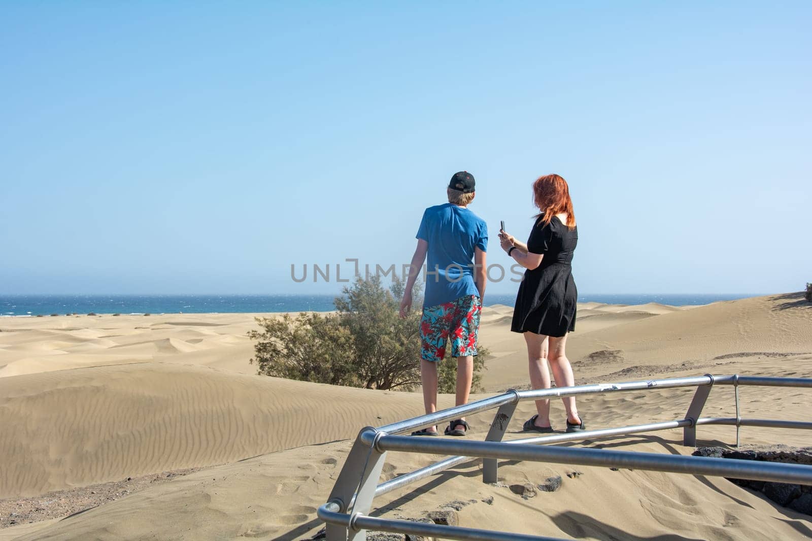 Two teenagers stand in the sand dunes of Maspalomas on Gran Canaria, Spain and look at the sea