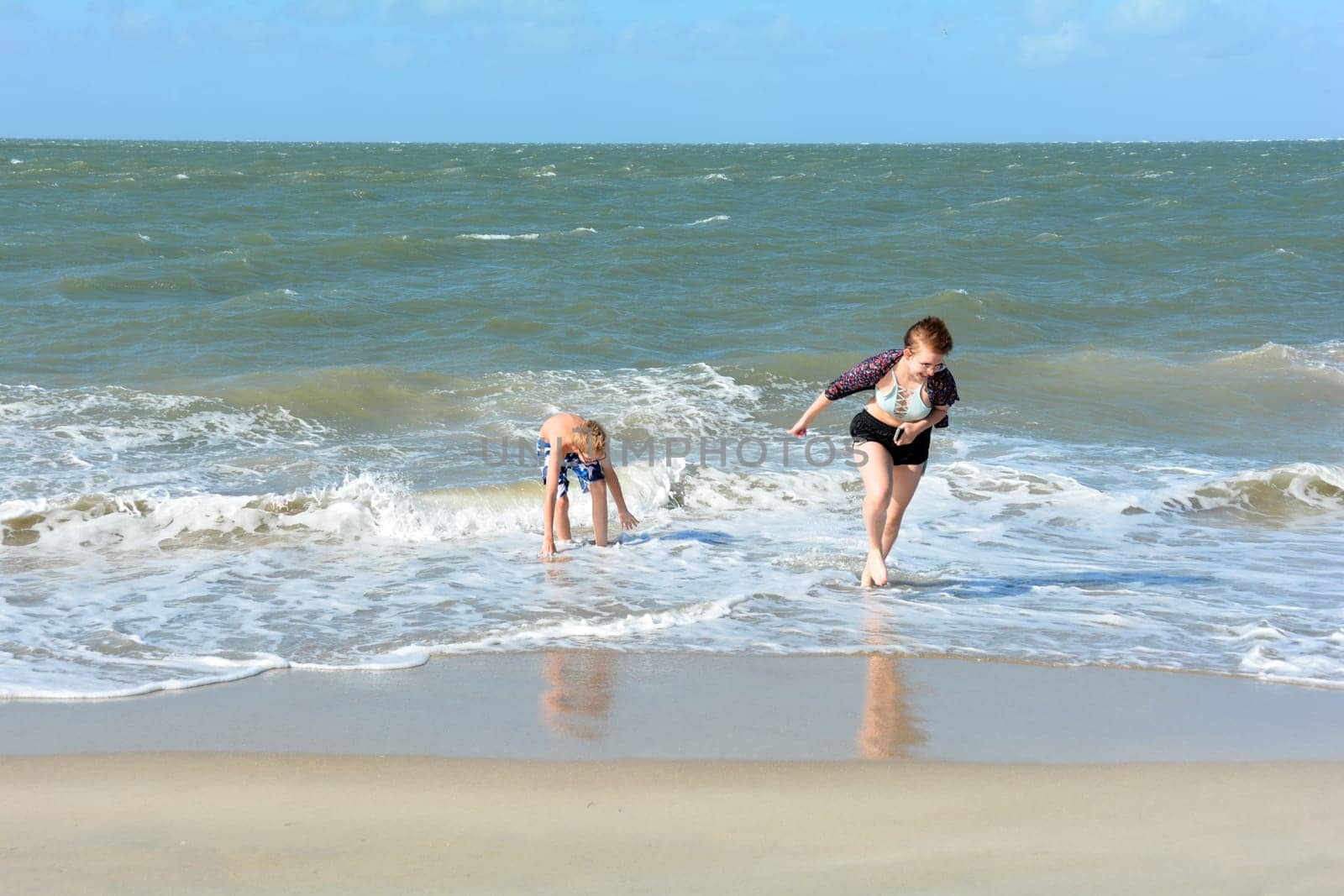 Two children have fun in the waves on the sea beach, Girl runs out of the water,Girl runs out of the water, boy plays in the waves