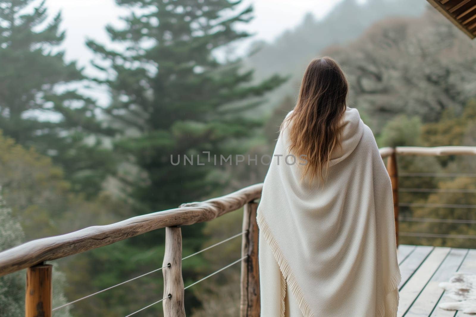 Beautiful woman wrapped in blanket standing on terrace of wooden house in the pine forest resort.