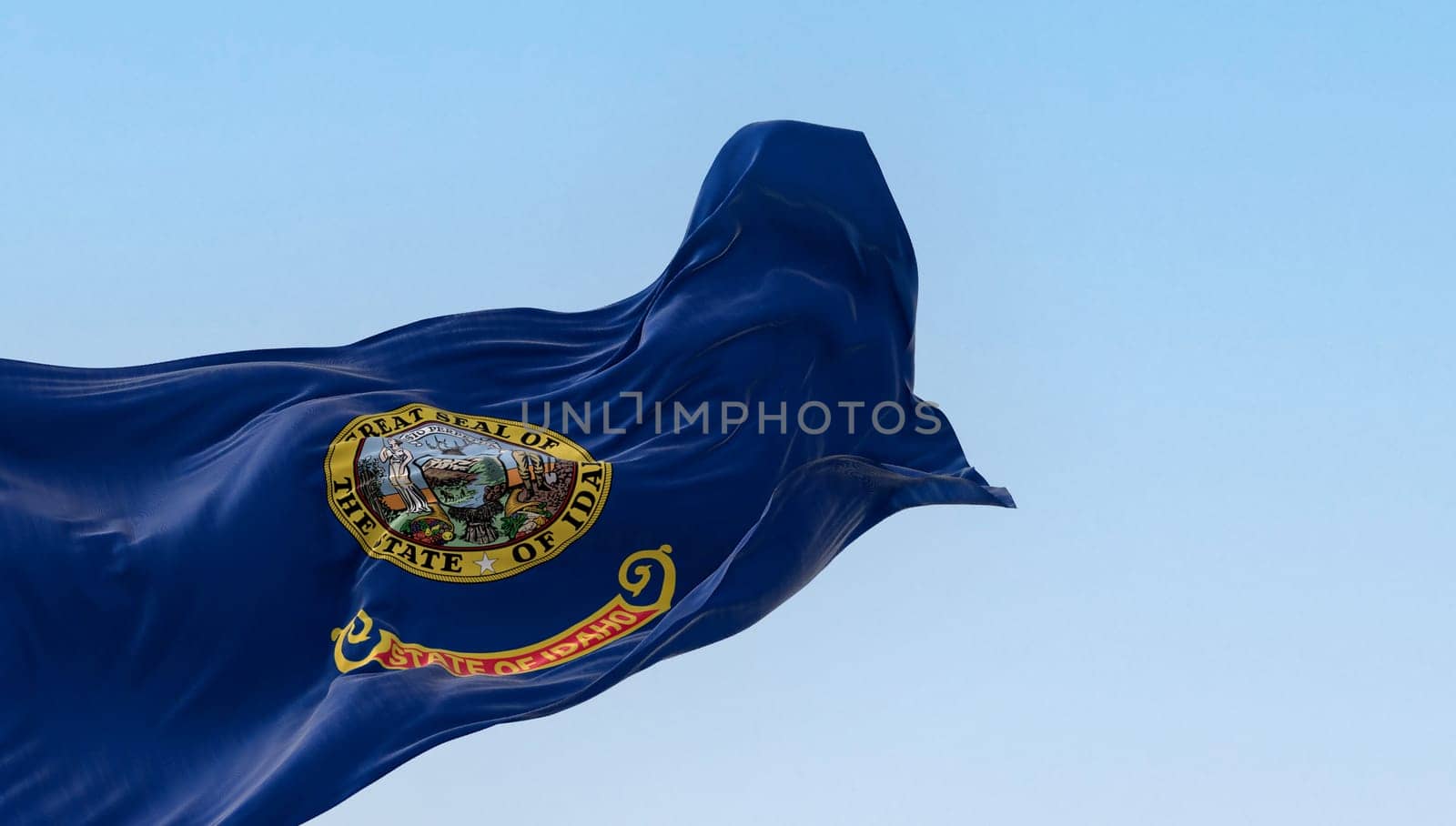 Idaho state flag fluttering in the wind. Blue background with the state seal and a red band with State of Idaho in gold text. 3d illustration render. Selective focus. Close-up