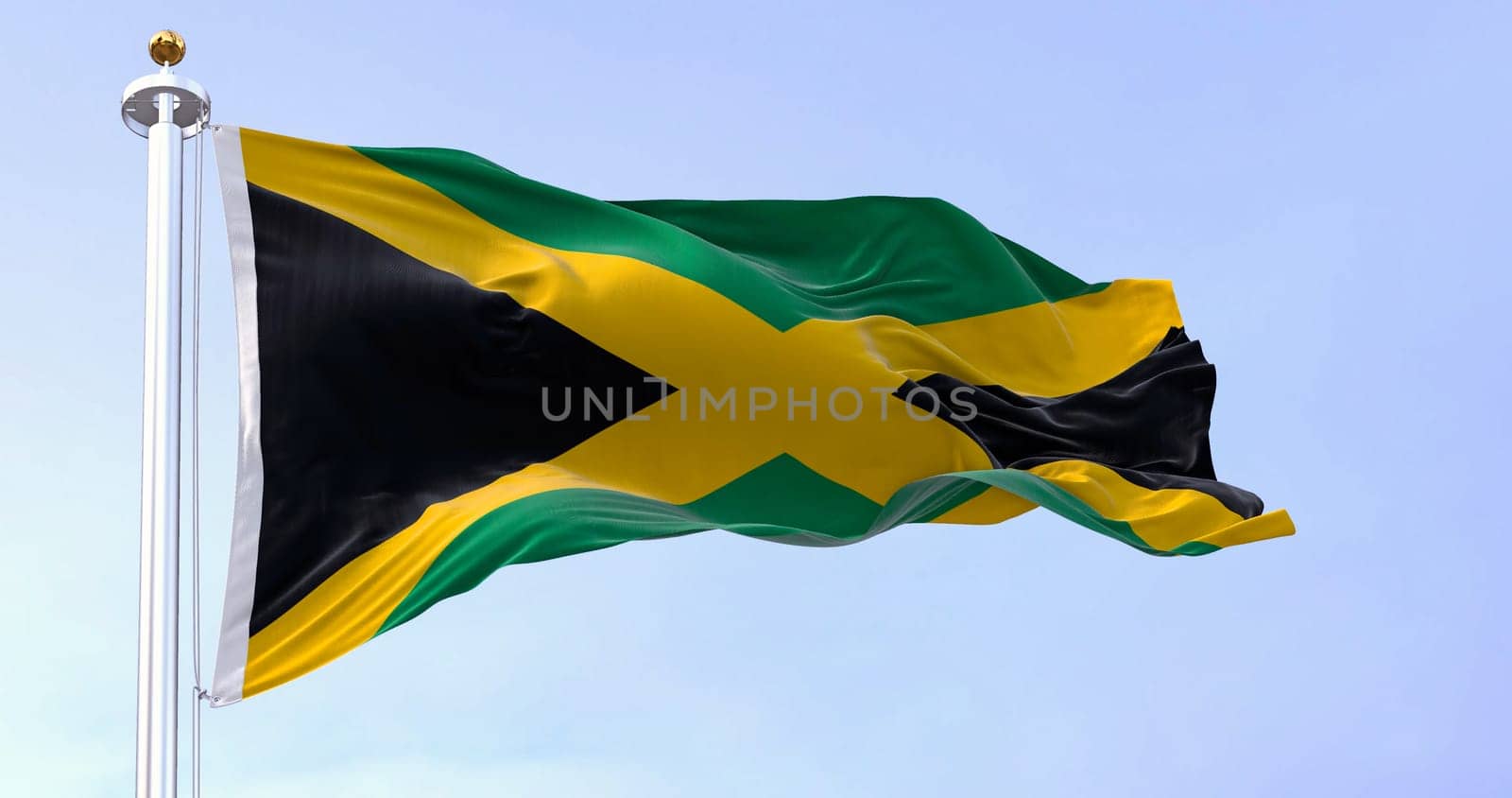 Jamaica national flag waving in the wind on a clear day. Gold saltire dividing it into four sections: two green and two black. 3d illustration render. Fluttering fabric. Selective focus