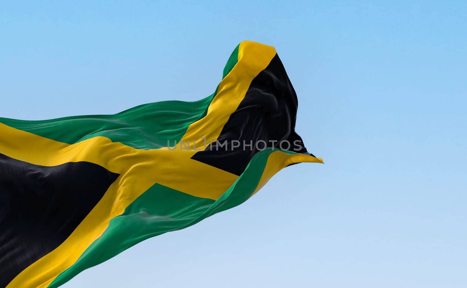 Jamaica national flag waving in the wind on a clear day. Gold saltire dividing it into four sections: two green and two black. 3d illustration render. Fluttering fabric. Selective focus