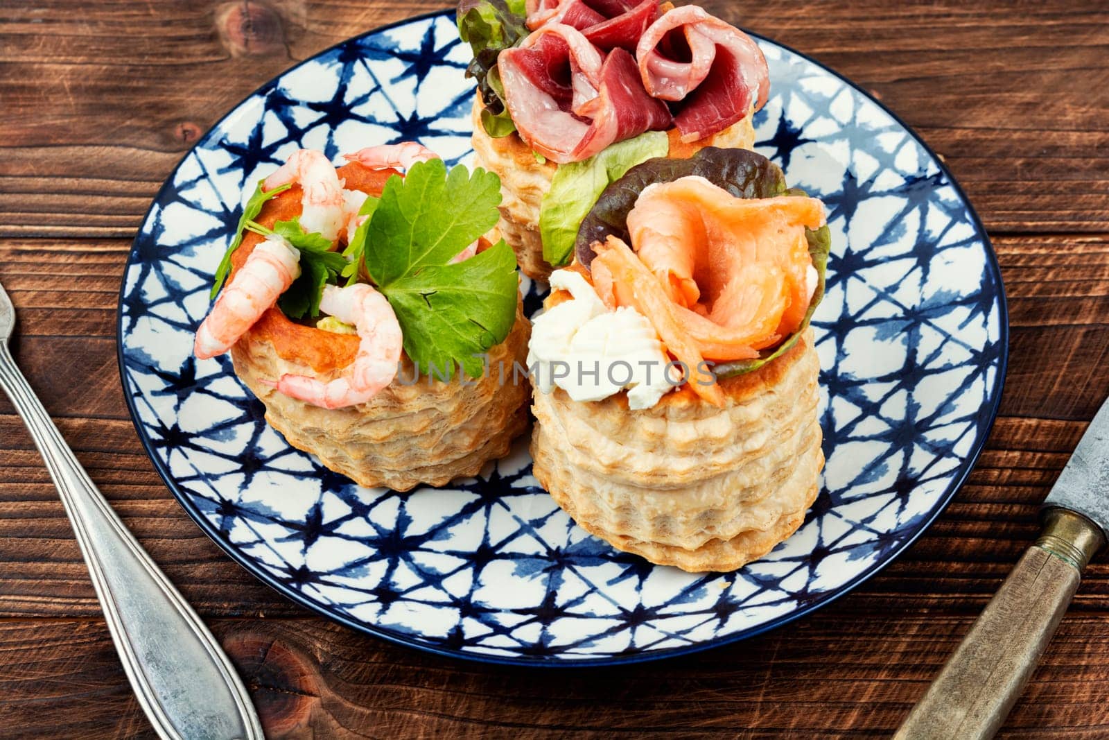 Puff pastry tartlets with fish, shrimp and bacon on a plate on the table.