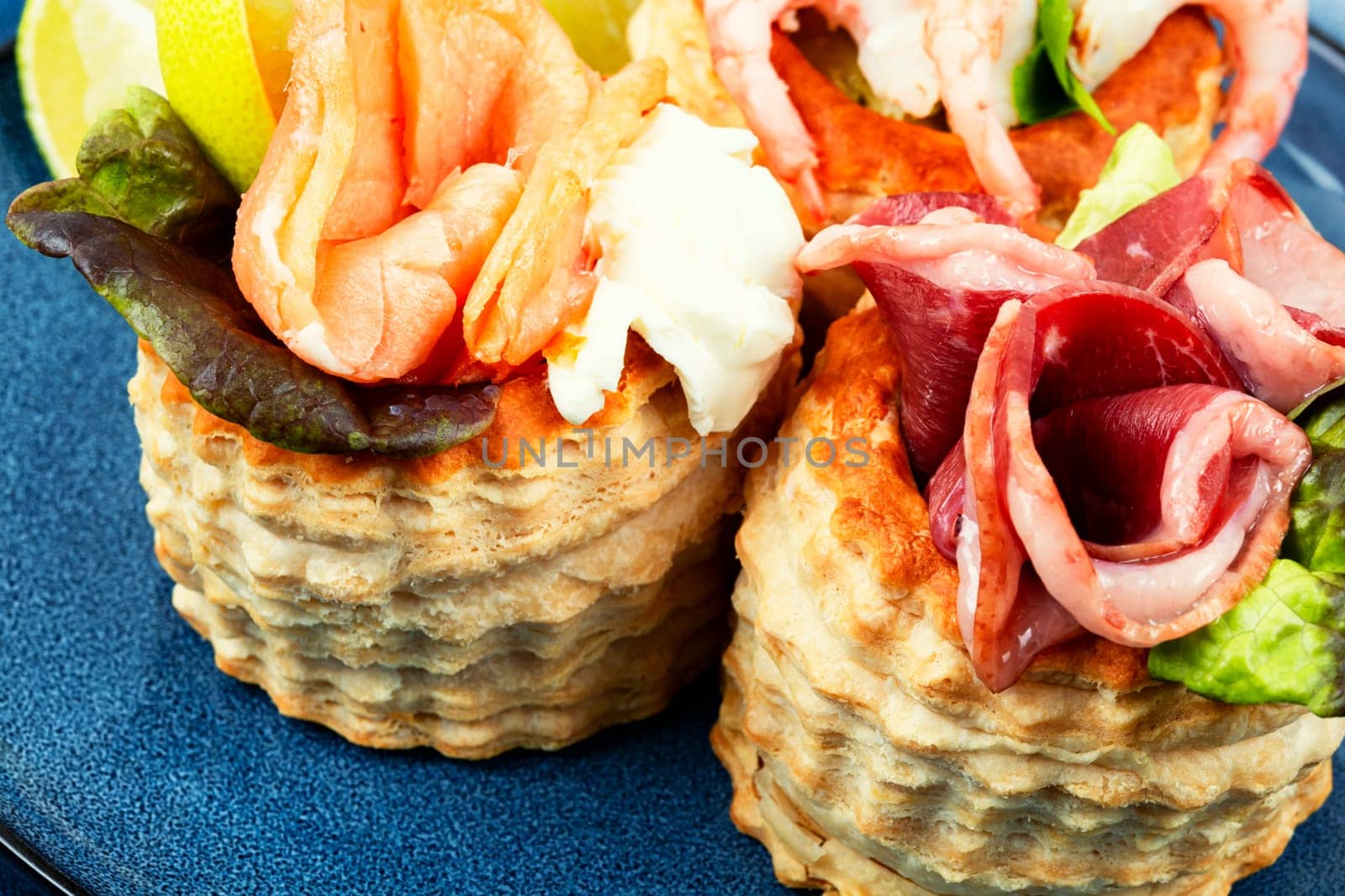 Puff pastry tartlets with fish, shrimp and bacon on a plate on the table.