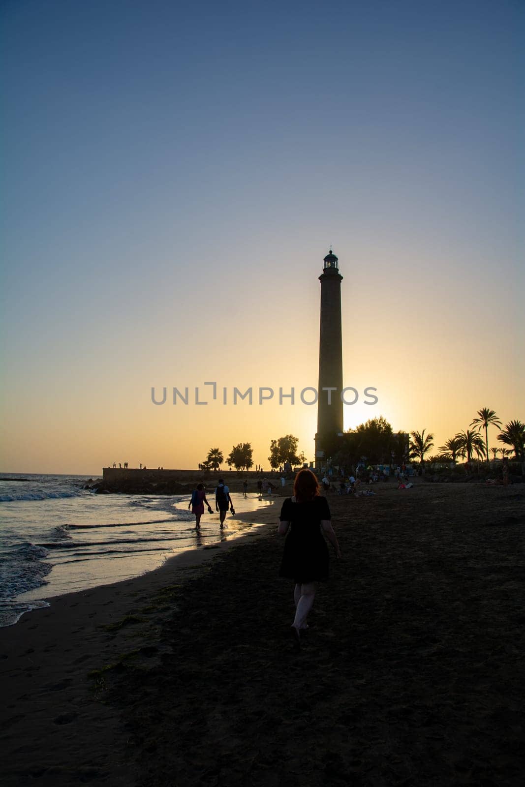 Lighthouse in Maspalomas ( Faro de Maspalomas ) on the Canary Island of Gran Canaria in Spain at sunset with a girl,sandy beach and sea