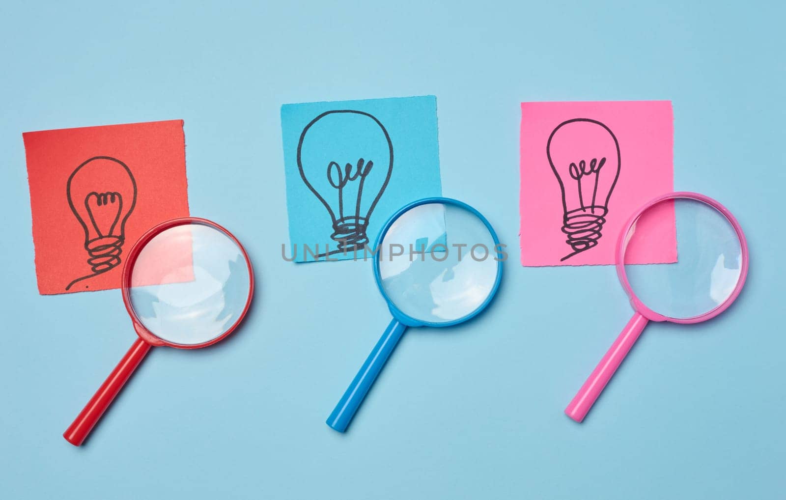 Drawn light bulbs on sheets of paper and a plastic magnifying glass, the concept of searching for new ideas