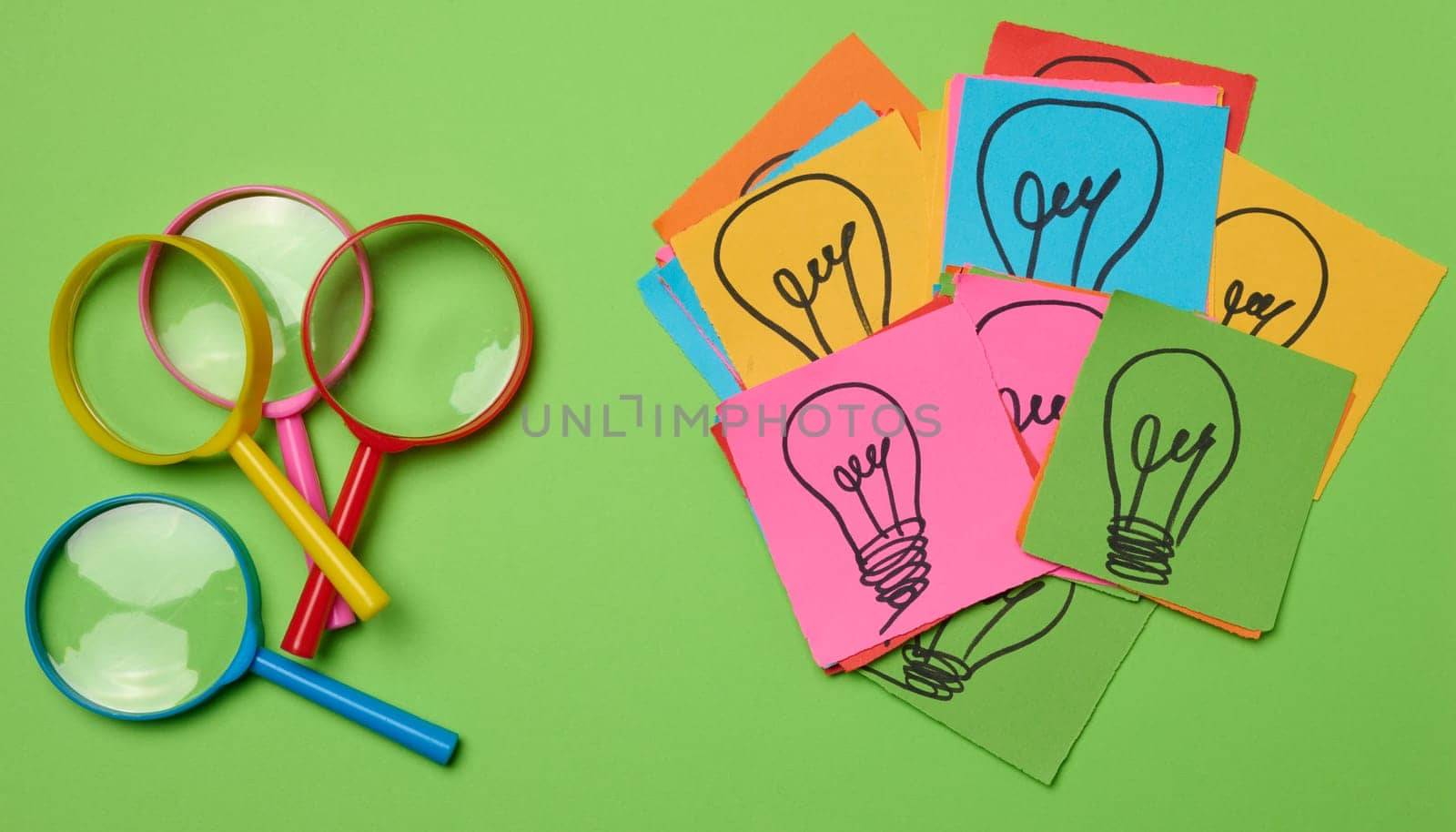 Drawn light bulbs on sheets of paper and a plastic magnifying glass, the concept of searching for new ideas.