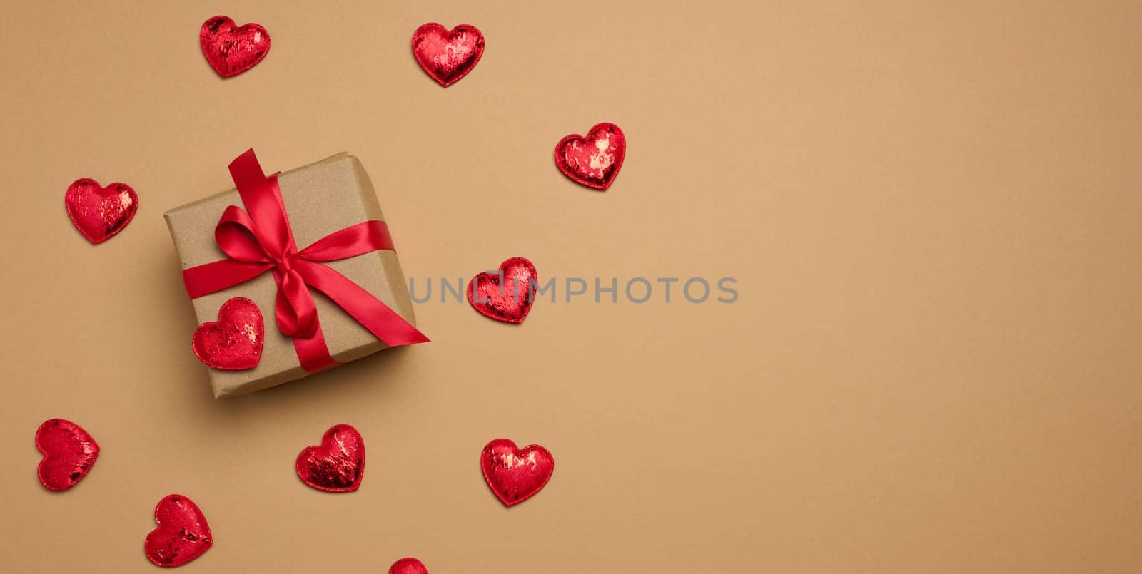 Box tied with a red ribbon and small hearts on a beige background, top view. Copy space