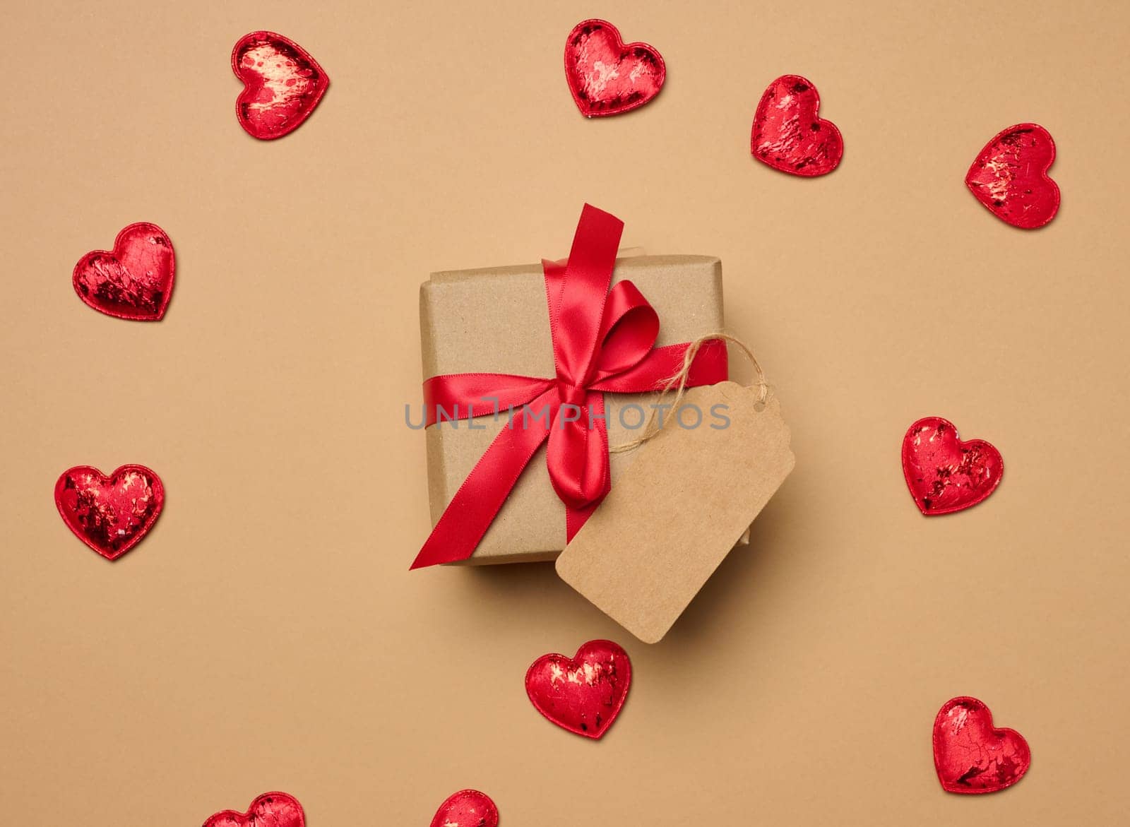 Box tied with a red ribbon and small hearts on a beige background, top view
