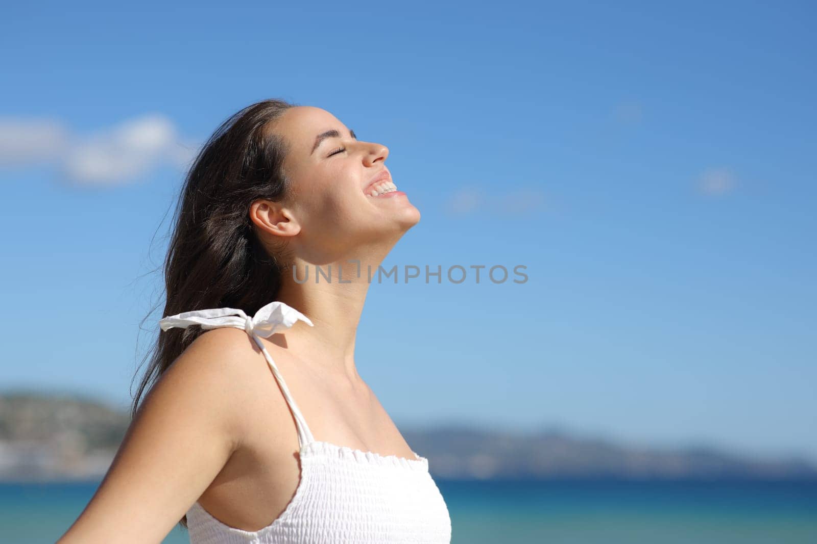 Happy woman in white dress breathing fresh air and laughing on the beach