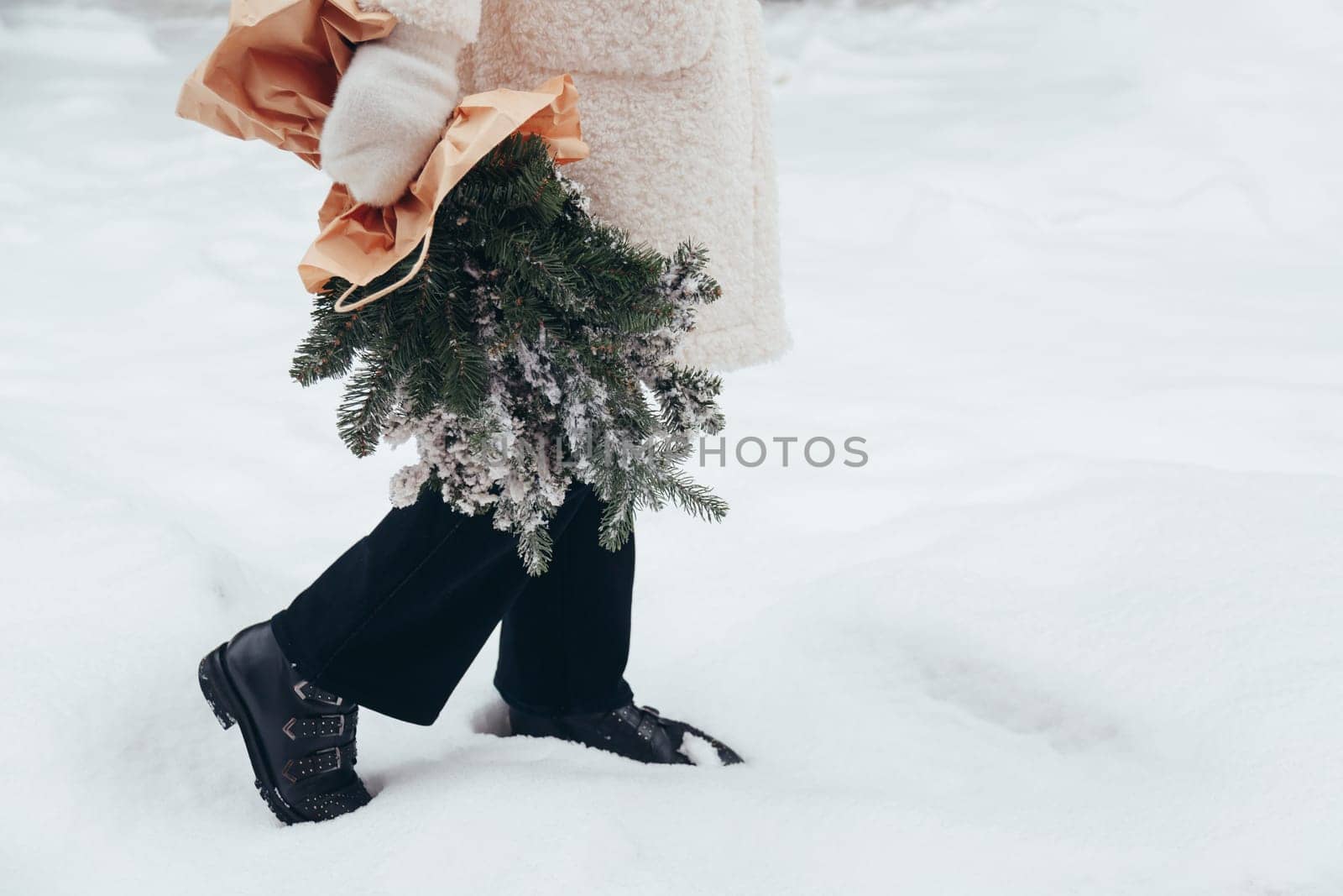 Girl in a white coat holds a Christmas pine branches bouquet in her hands.