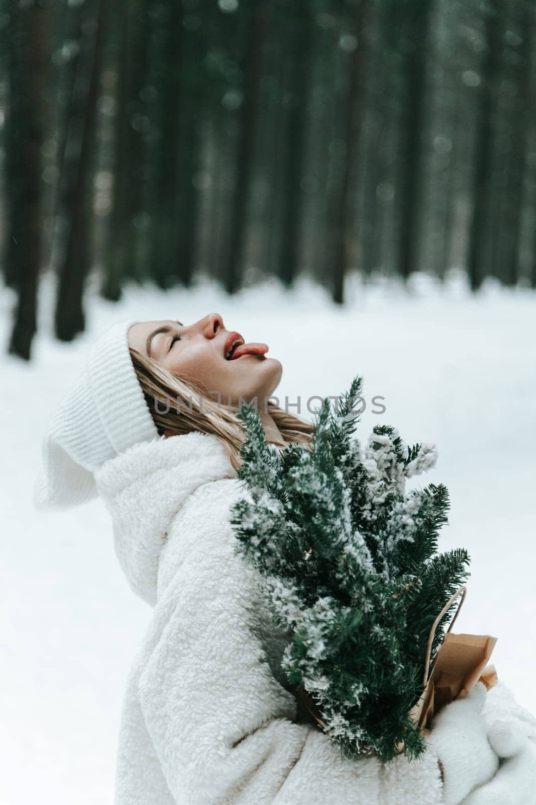 Happy young woman catching snowflakes with mouth in winter forest.