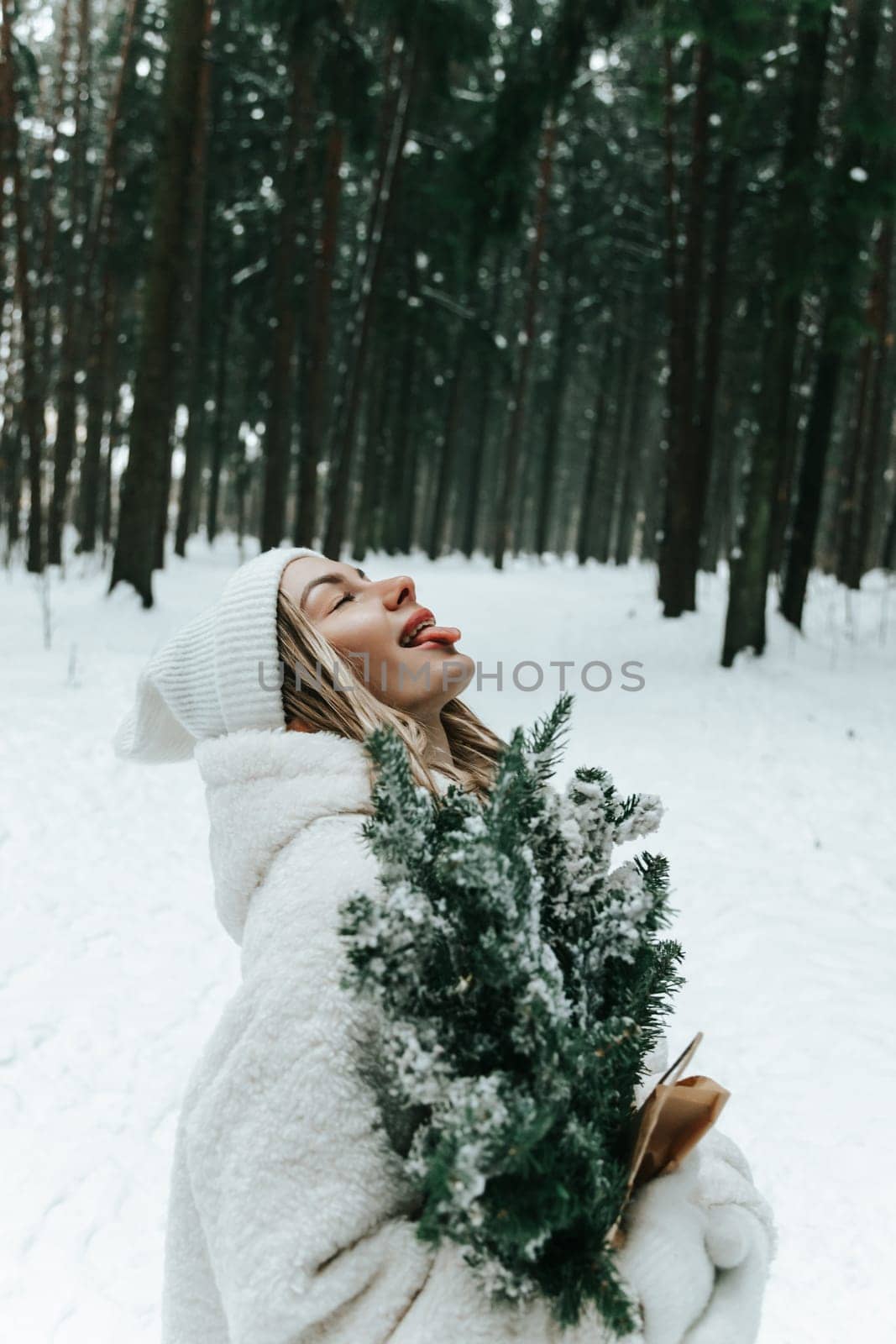 Happy young woman catching snowflakes with mouth in winter forest