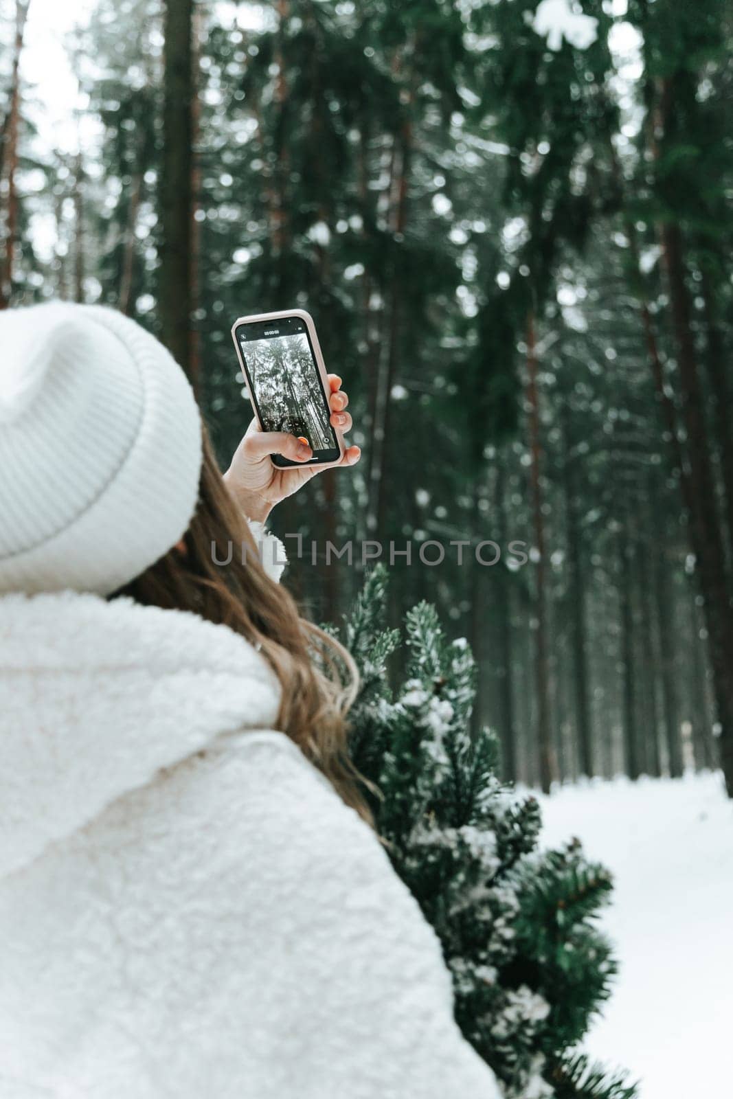 Young woman in a snowy forest with smartphone shooting video blog.
