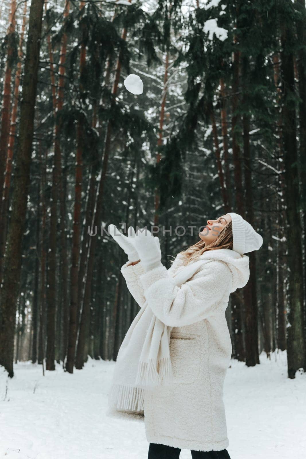 Woman in white clothes throw up a snowball in winter forest.