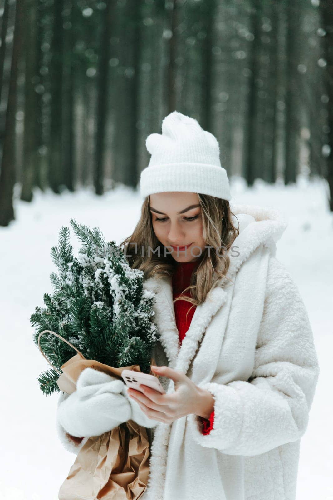 Young woman in a snowy forest with smartphone chatting online outdoors in the wild.