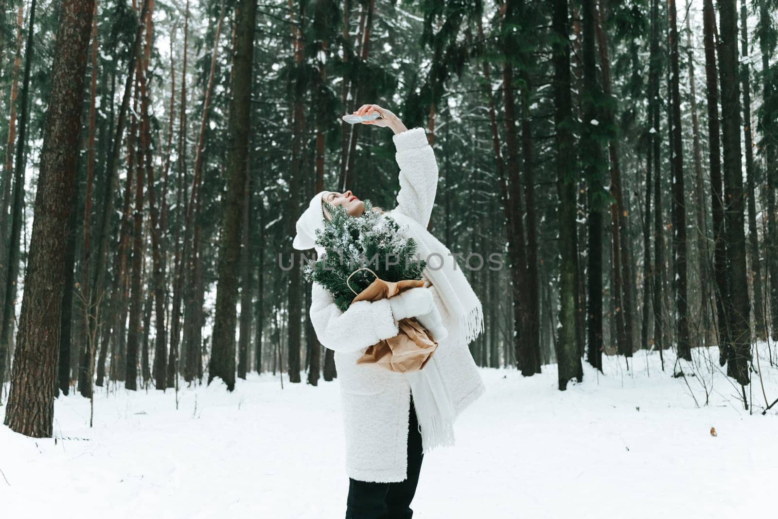 Young woman in a snowy forest rise up smartphone searching for a connection, video chat online outdoors in the wild.