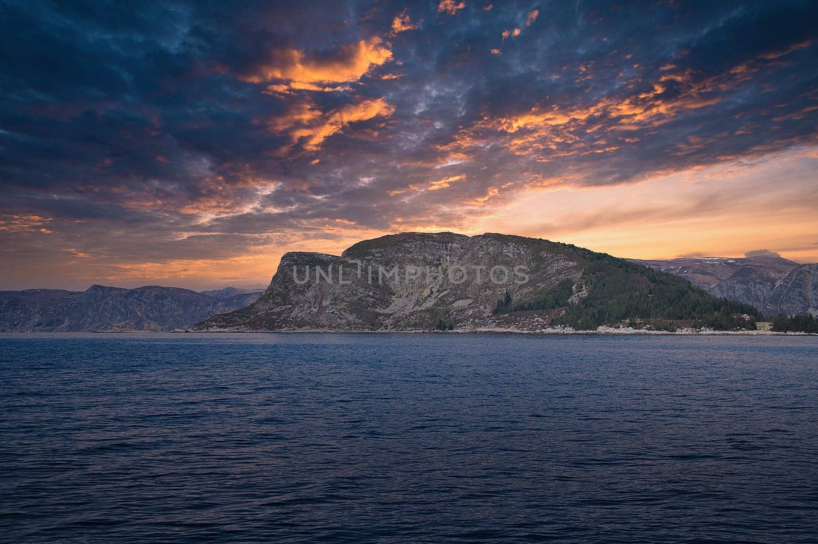 Westcap in Norway. Mountain that reaches into the fjord. Cloudy sky with clouds illuminated by the sun. Landscape shot from Scandinavia