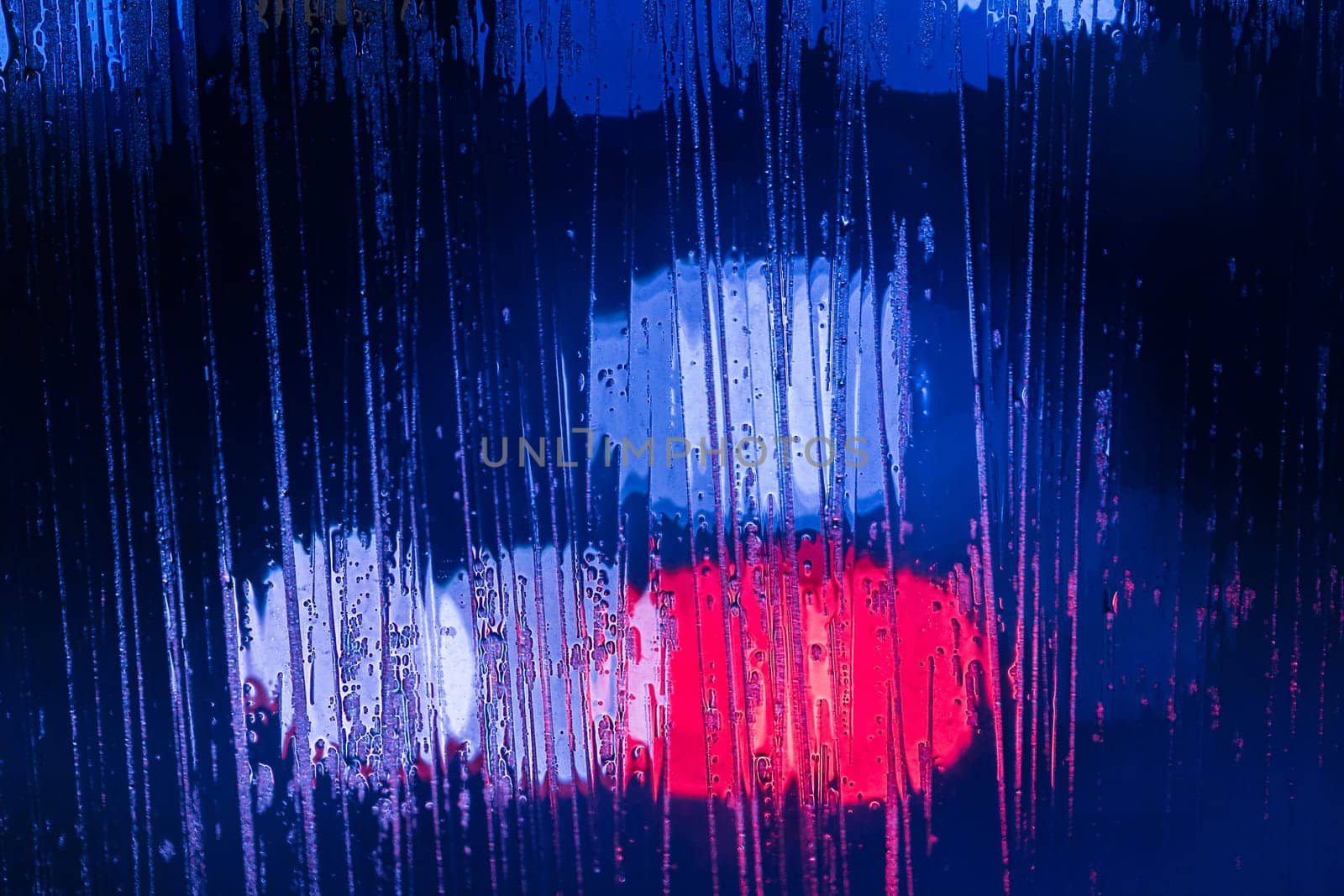 an abstract background of red and blue police lights bokeh trough wet glass at night close-up with selective focus by z1b
