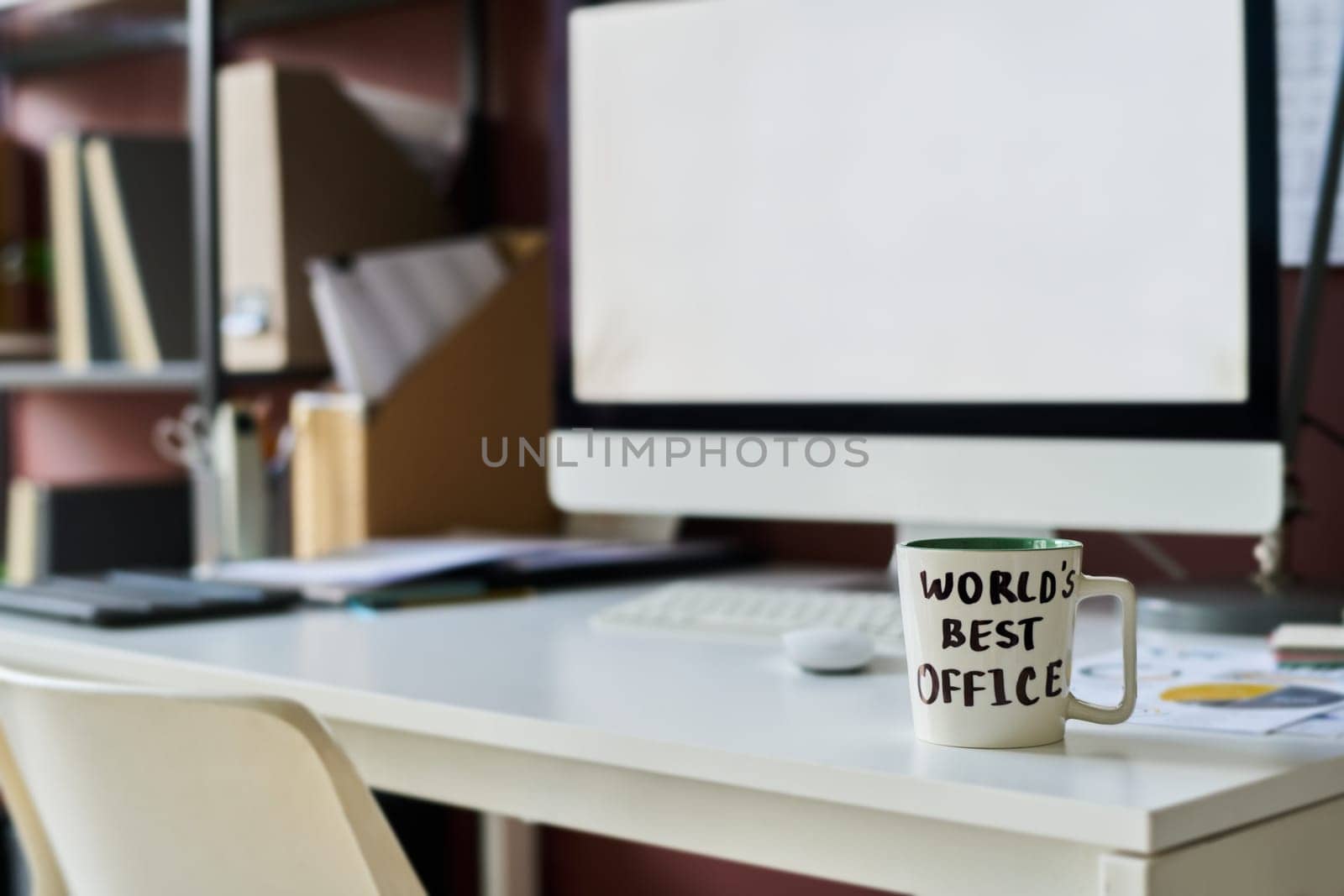 White mug with tea or coffee standing on workplace of economist or analyst against computer monitor with blank screen