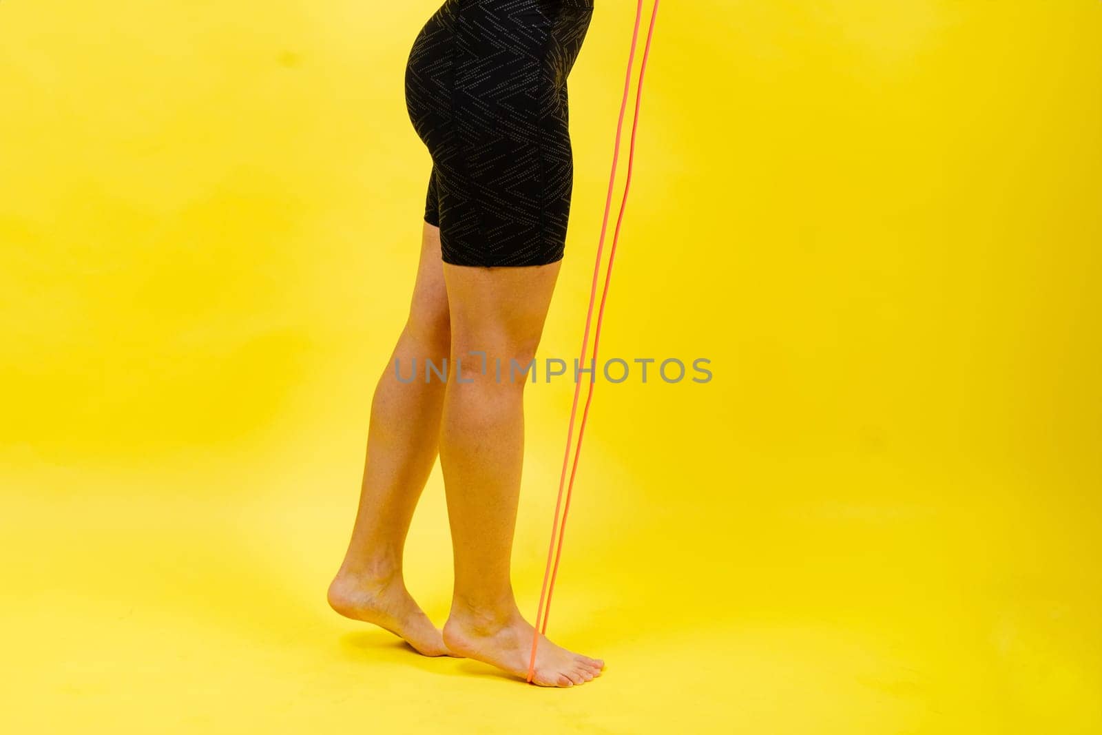 Fit female athlete with jumping with rope during fitness training against yellow background