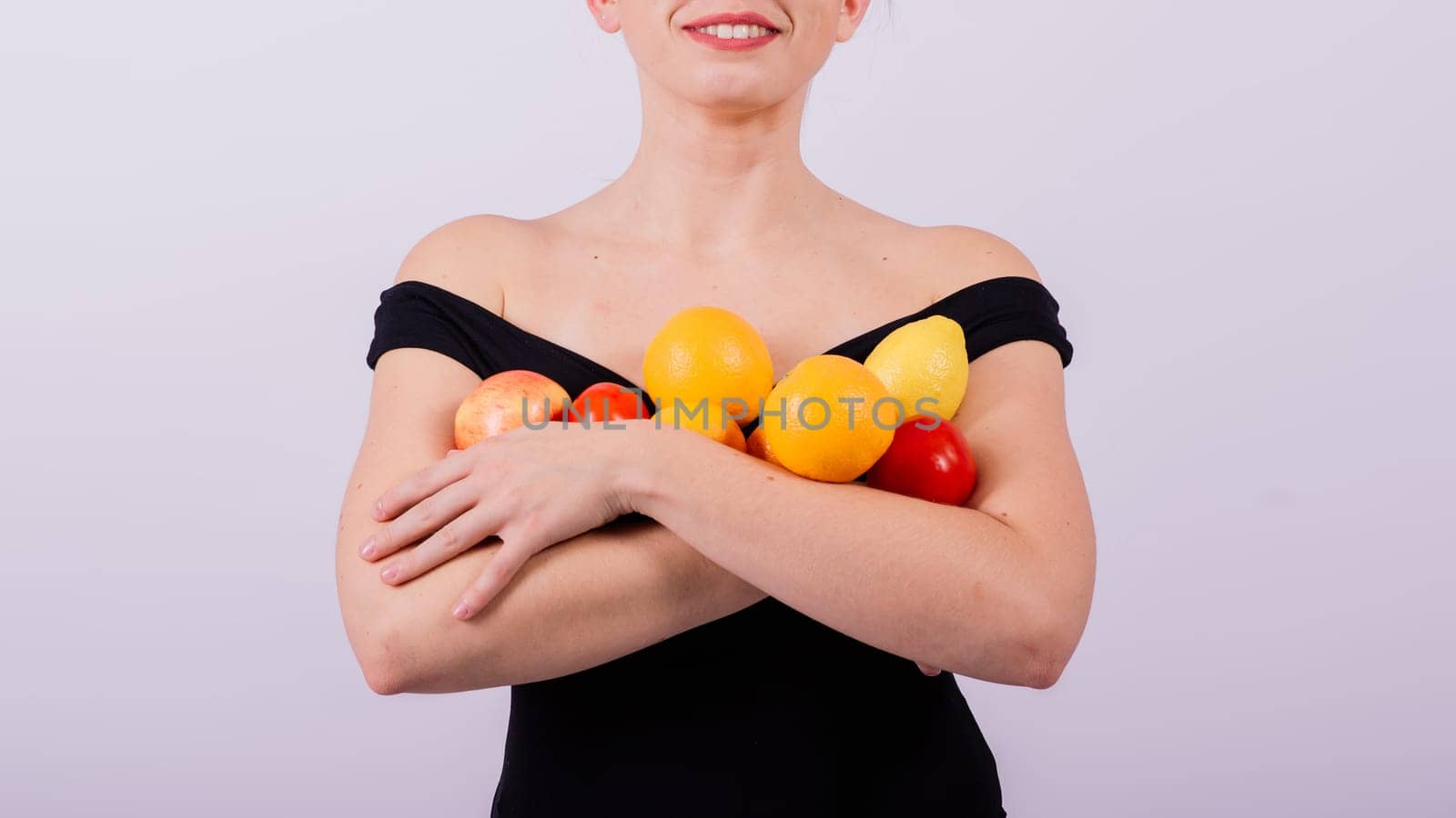 A female holding an apples, lemons, oranges in different arms isolated on grey background.