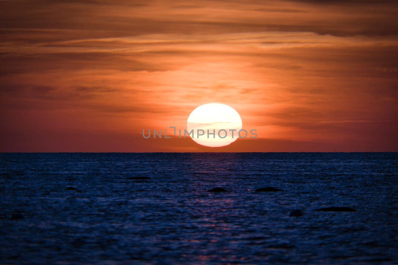 Sunset over the Baltic Sea. The red sun sinks into the sea. Evening atmosphere on the coast. Landscape photograph in northern Germany
