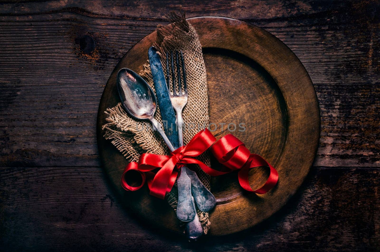 Valentines dinner setting with vintage silverware, dinner plate and red ribbon on wooden table. Valentine day background frame for special romantic dining celebration. Top view.
