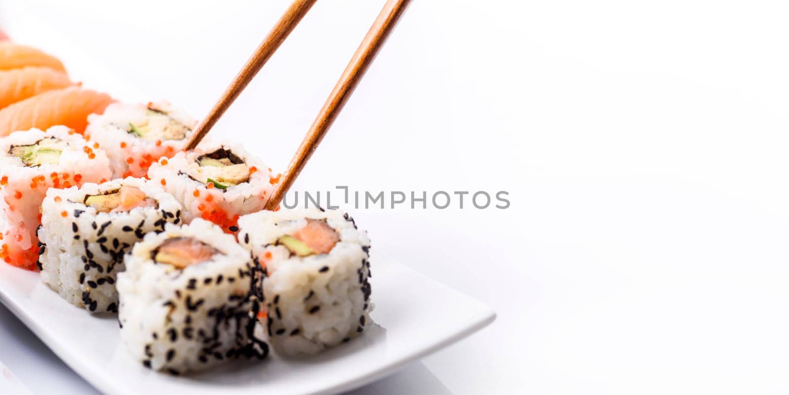 Closeup of sushi roll dish with bamboo chopstick frame isolated on white background. Luxury japanese restaurant dinner with sashimi, maki, surimi and soy sauce on plate. Classy Japan food bites with tuna fish, seafood, salmon, avocado and caviar.
