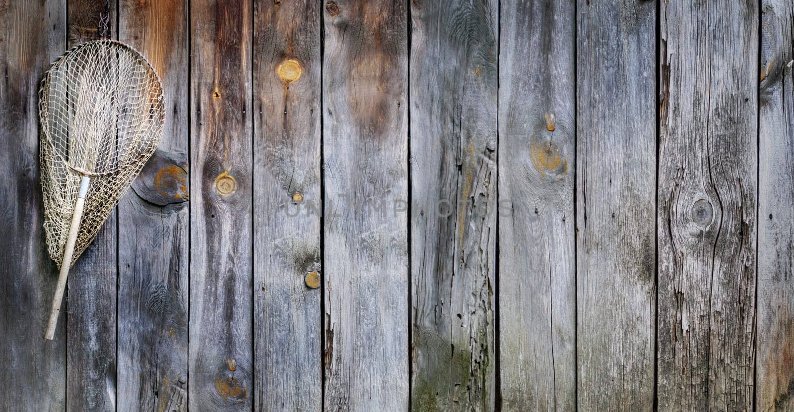 Fishing concept. Old fisherman equipment on vintage wooden background with copyspace. Landing net hooked on rustic board.