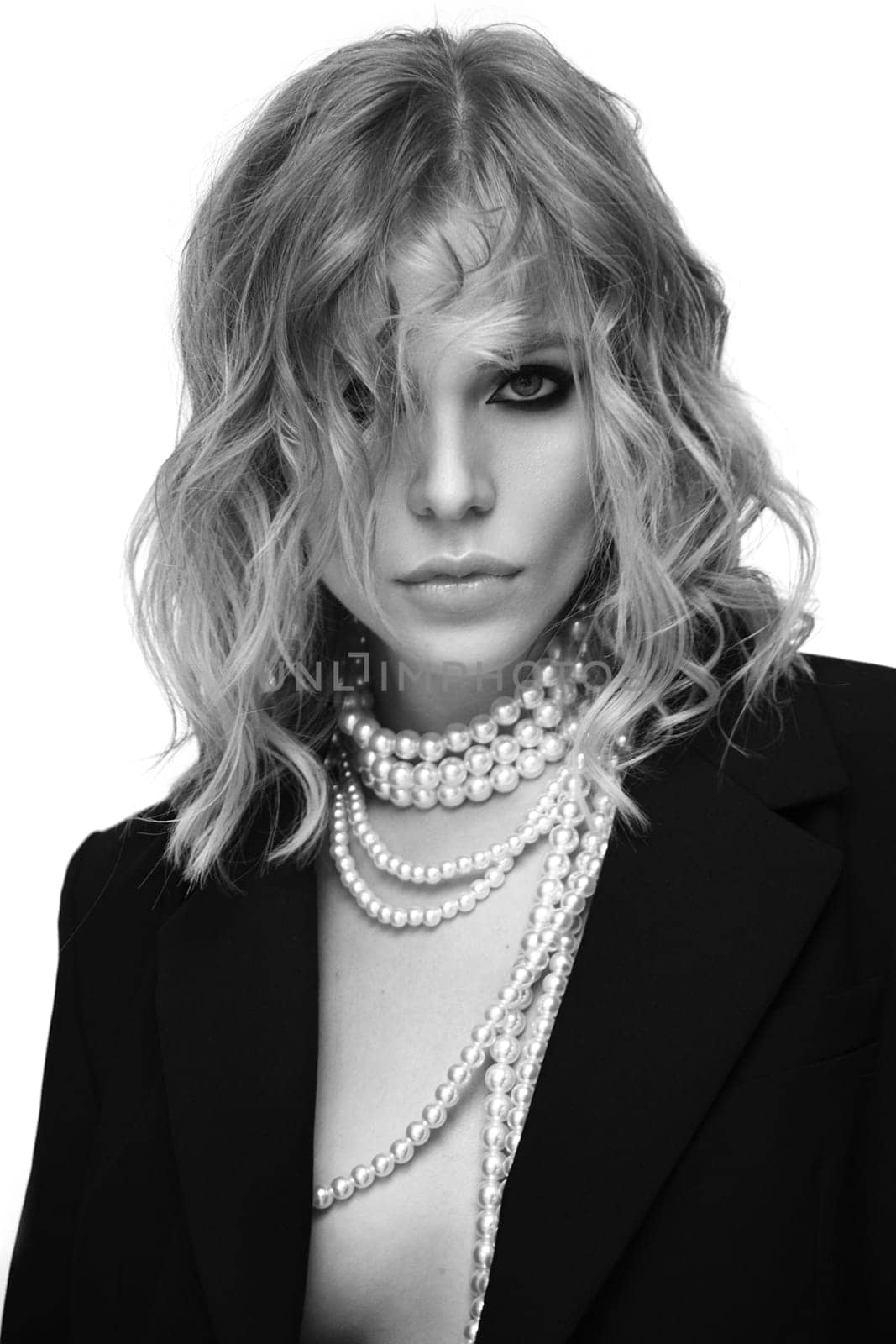 A beautiful woman with loose hair, in a jacket and beads, poses in the studio on a white background.