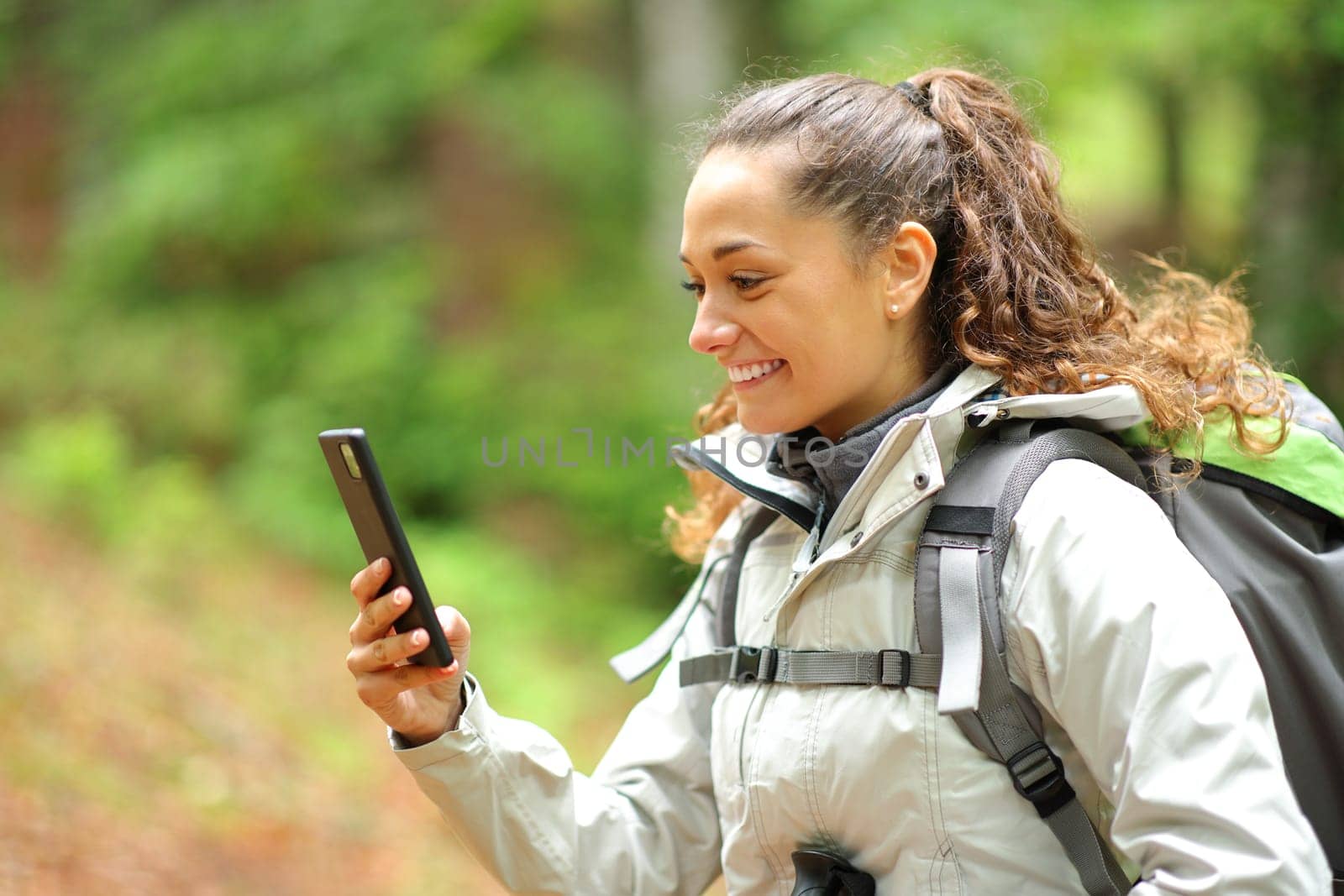 Happy hiker checking cell phone walking in a forest