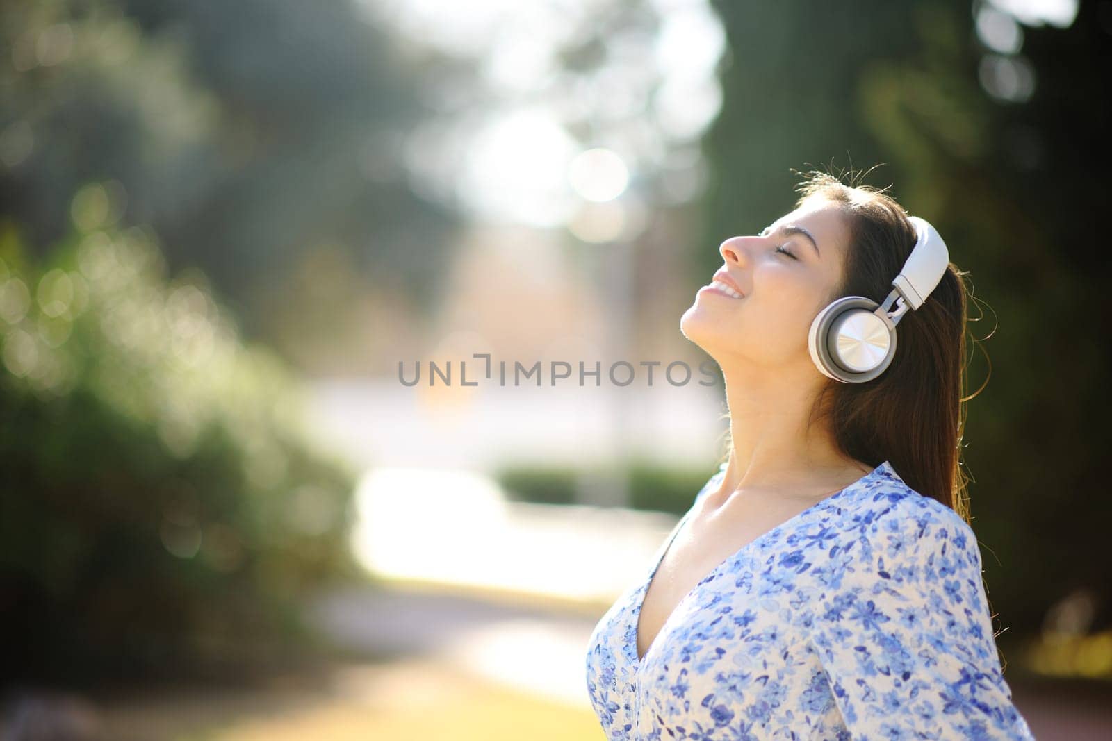 Side view portrait of a happy woman listening audiobook meditating with headphone in a park