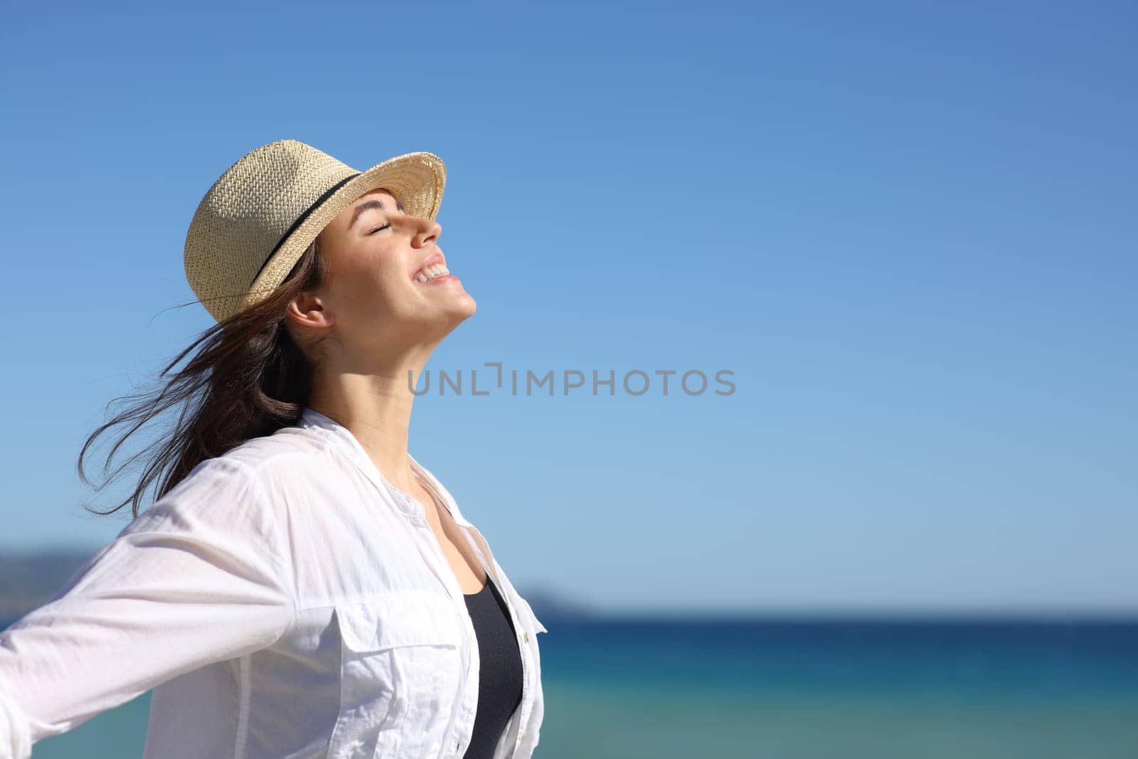 Side view portrait of a happy woman on the beach breathing fresh air wearing hat a summer sunny day