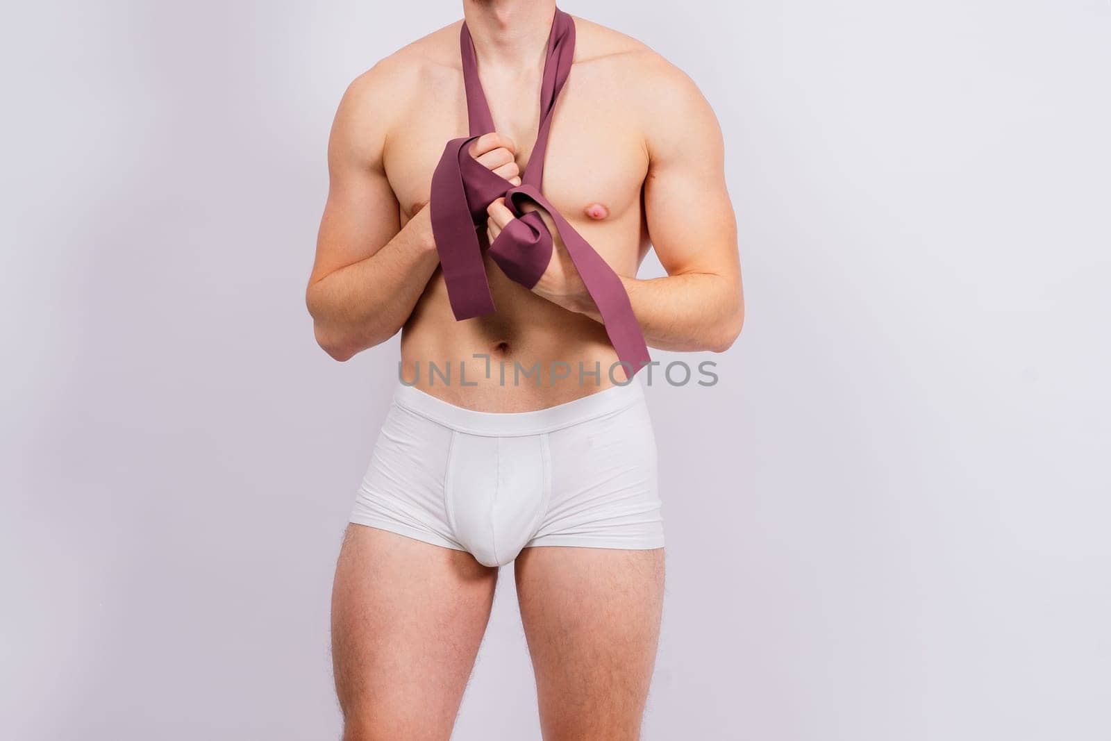 Athlete with muscular body in white panties is doing physical exercises with rubber