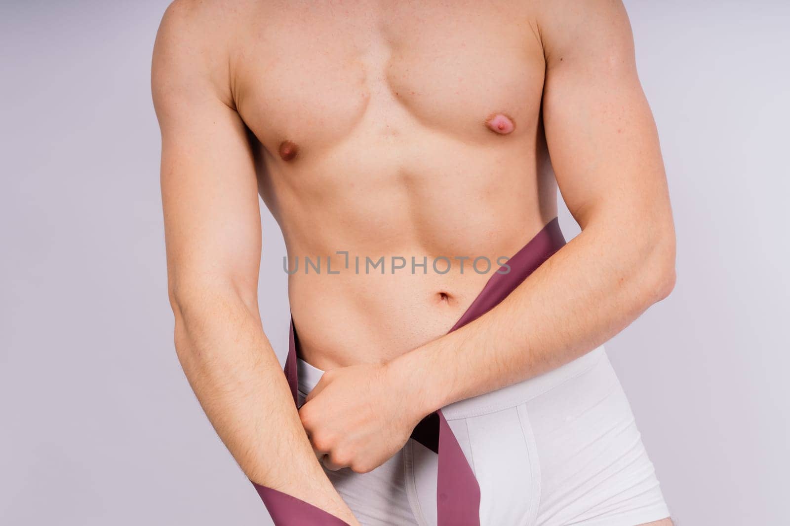 Athlete with muscular body in white panties is doing physical exercises with rubber