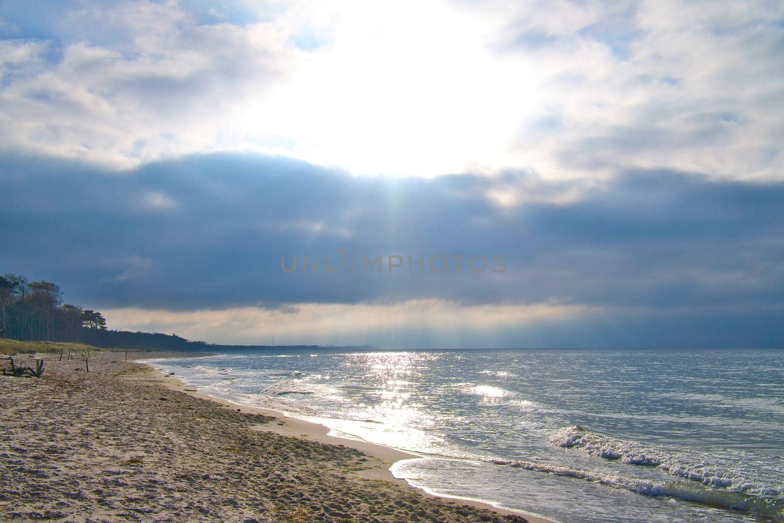 Sunset on the west beach on the Baltic Sea. Waves, beach, cloudy sky and the last rays of sunshine on the coast. Landscape photo