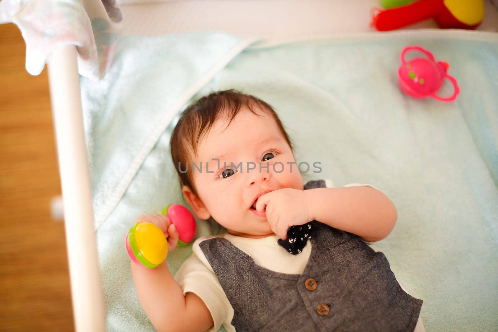 baby,lying,awake,crib,top view,white skin,suit,toys