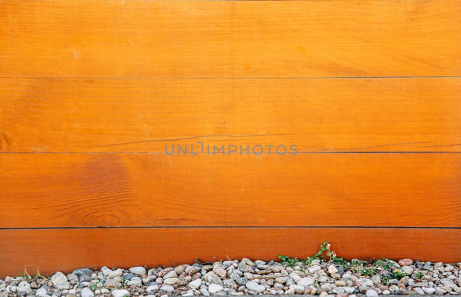 A horizontal wooden board of brown color with knots on the surface and small stones at the bottom.Texture or background