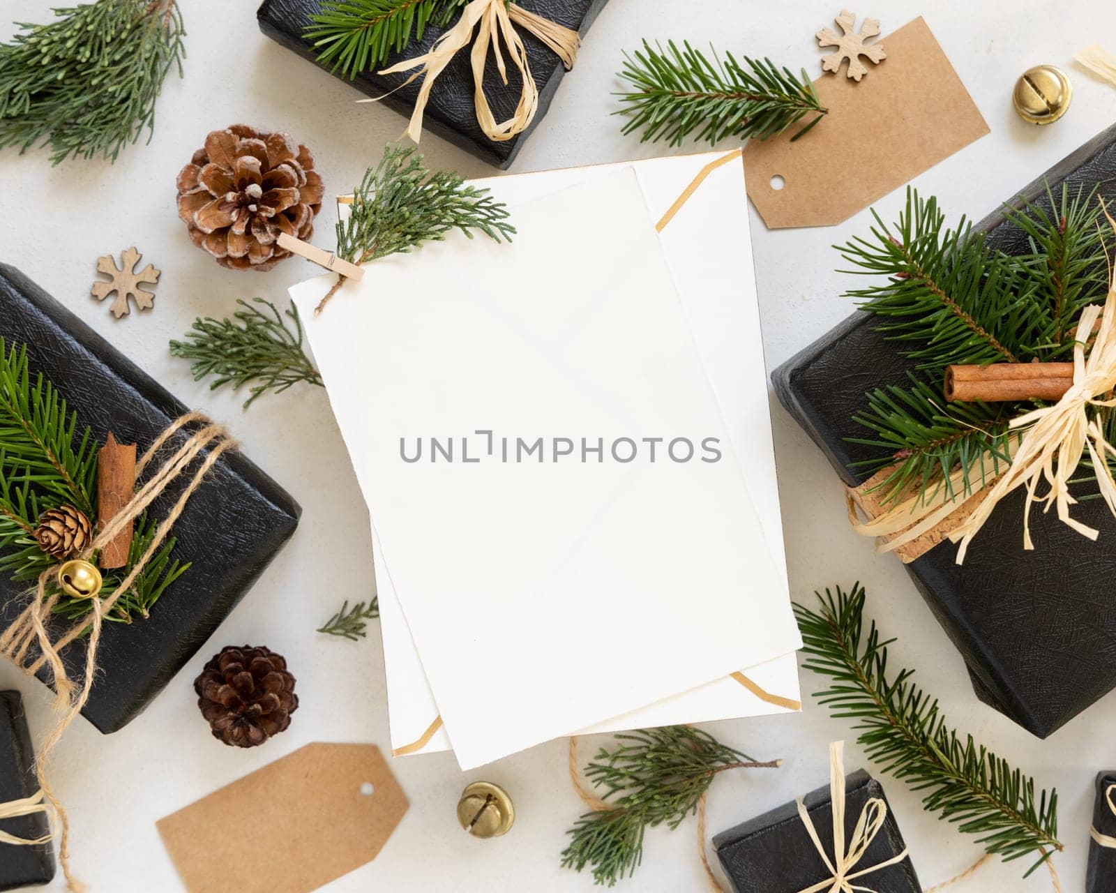 Paper card between Christmas decor, black gift boxes and green fir branches top view. Vertical blank card mockup, flat lay, copy space. Christmas or New Year Holiday greeting card