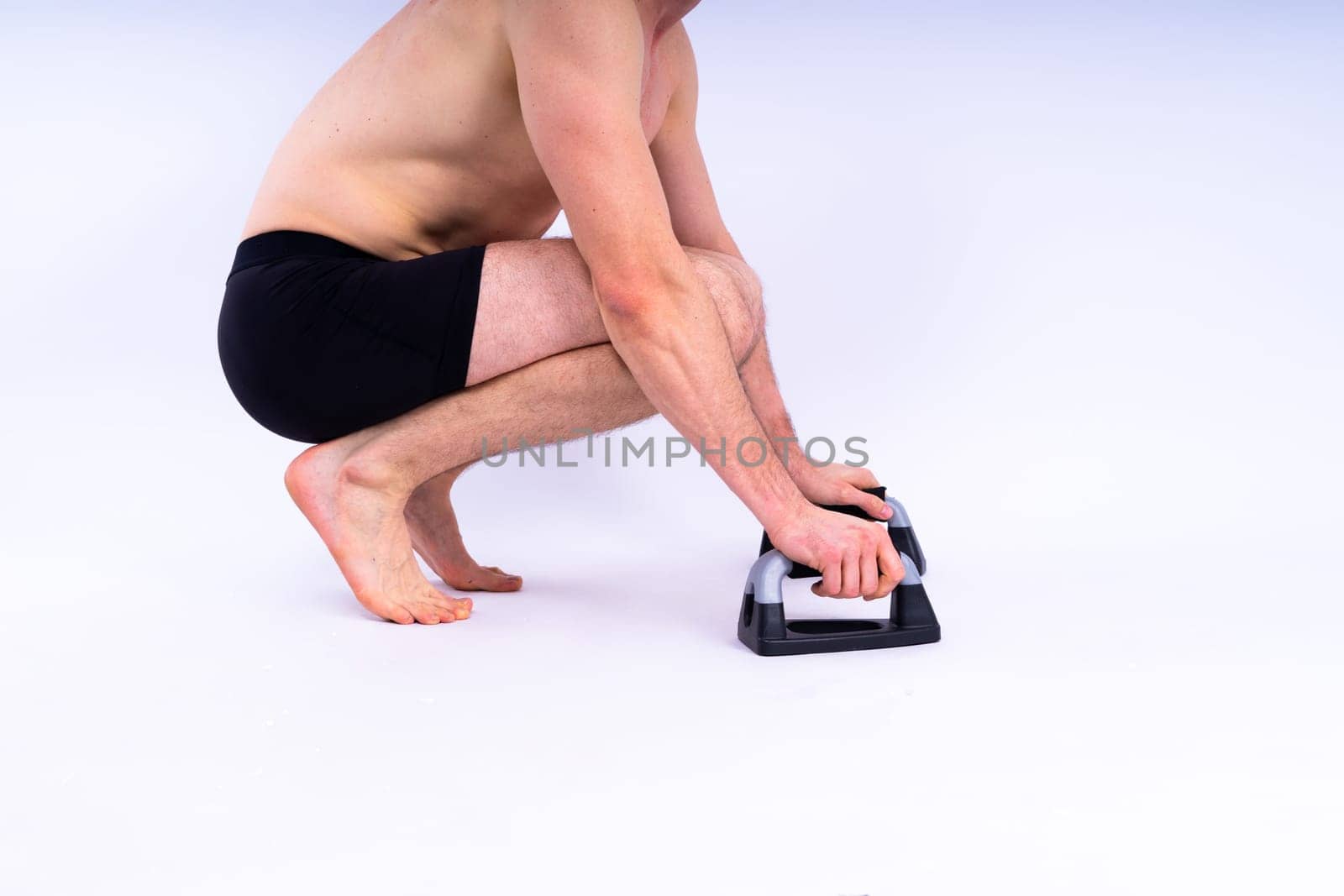 Shirtless muscular athlete do push-up on push up bars. Full body man on white studio background.