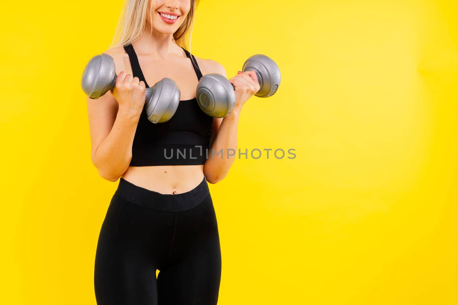 Athletic woman in a sportswear raises dumbbells leads healthy lifestyle has happy expression