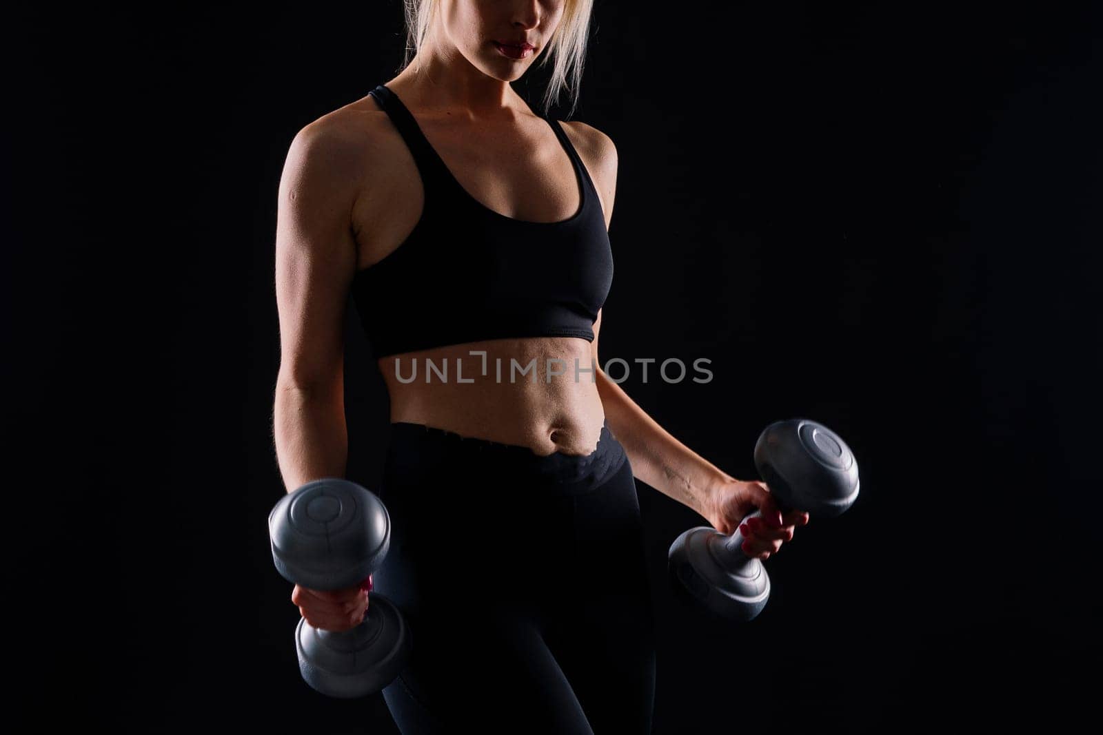 Athletic woman in a sportswear raises dumbbells leads healthy lifestyle has happy expression