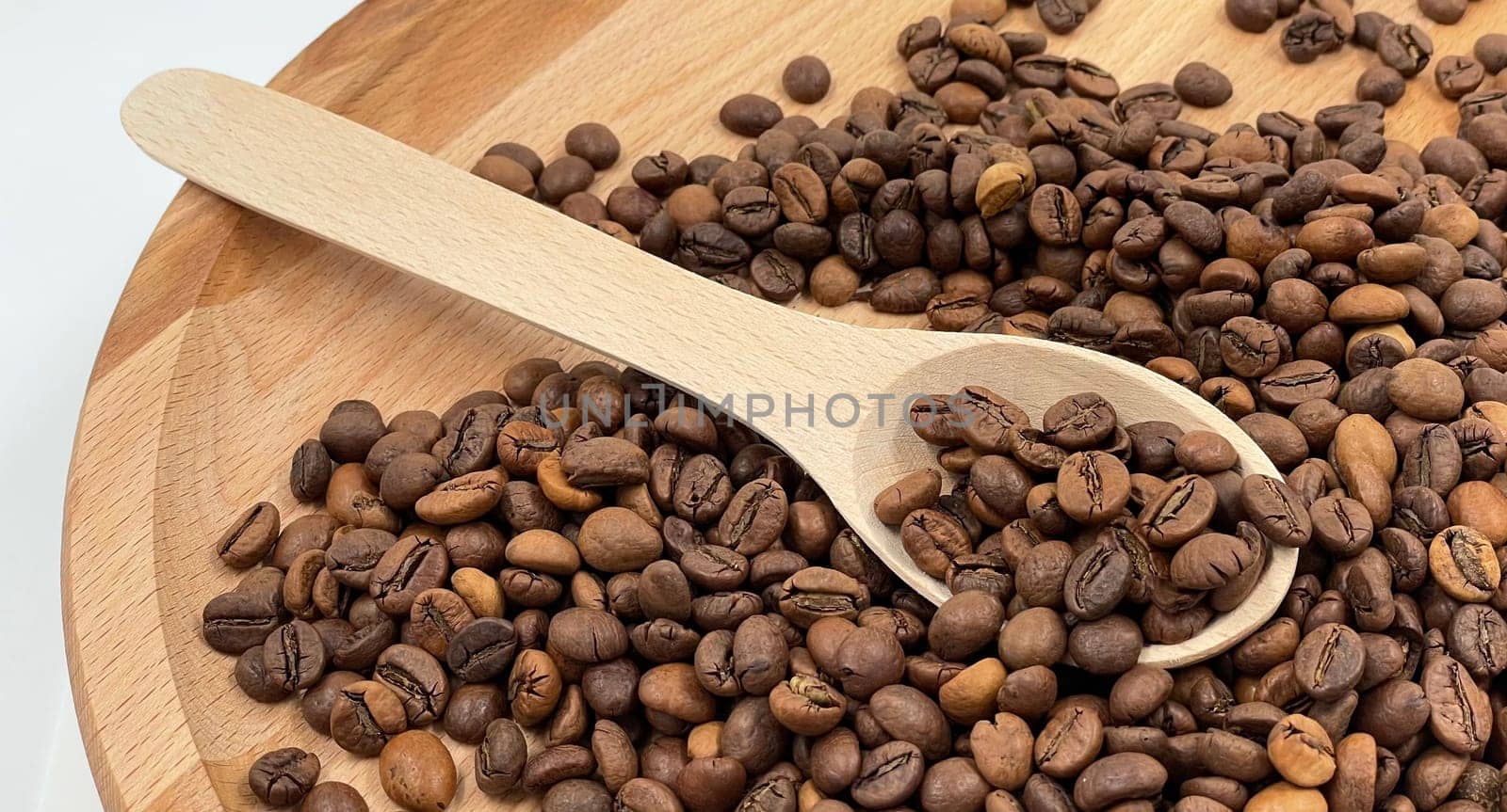 Top view of a pile of scattered aromatic roasted brown coffee beans with a wooden scoop. Coffee beans in a wooden spoon. Fragrant coffee, coffee drinks