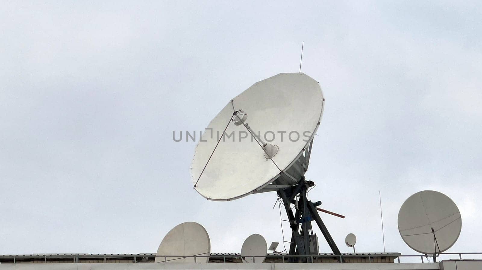 A group of large terrestrial satellites are pointed upward, a large satellite dish searches the sky during the day. Communication system. A television station or studio with large satellite dishes