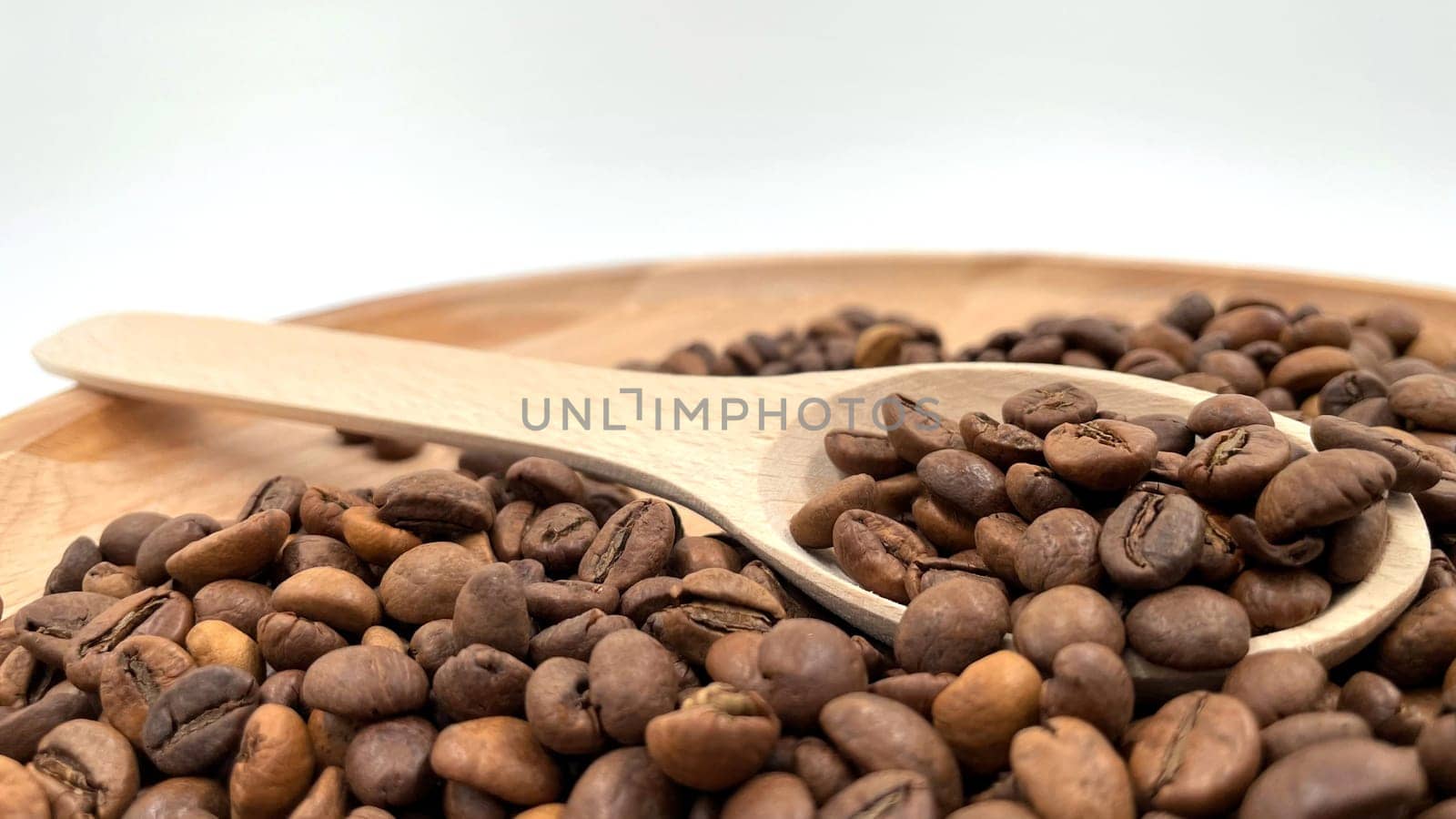 Food background texture of roasted coffee beans with a full shovel. A pile of scattered aromatic roasted brown coffee beans with a wooden scoop. Coffee beans in a wooden spoon