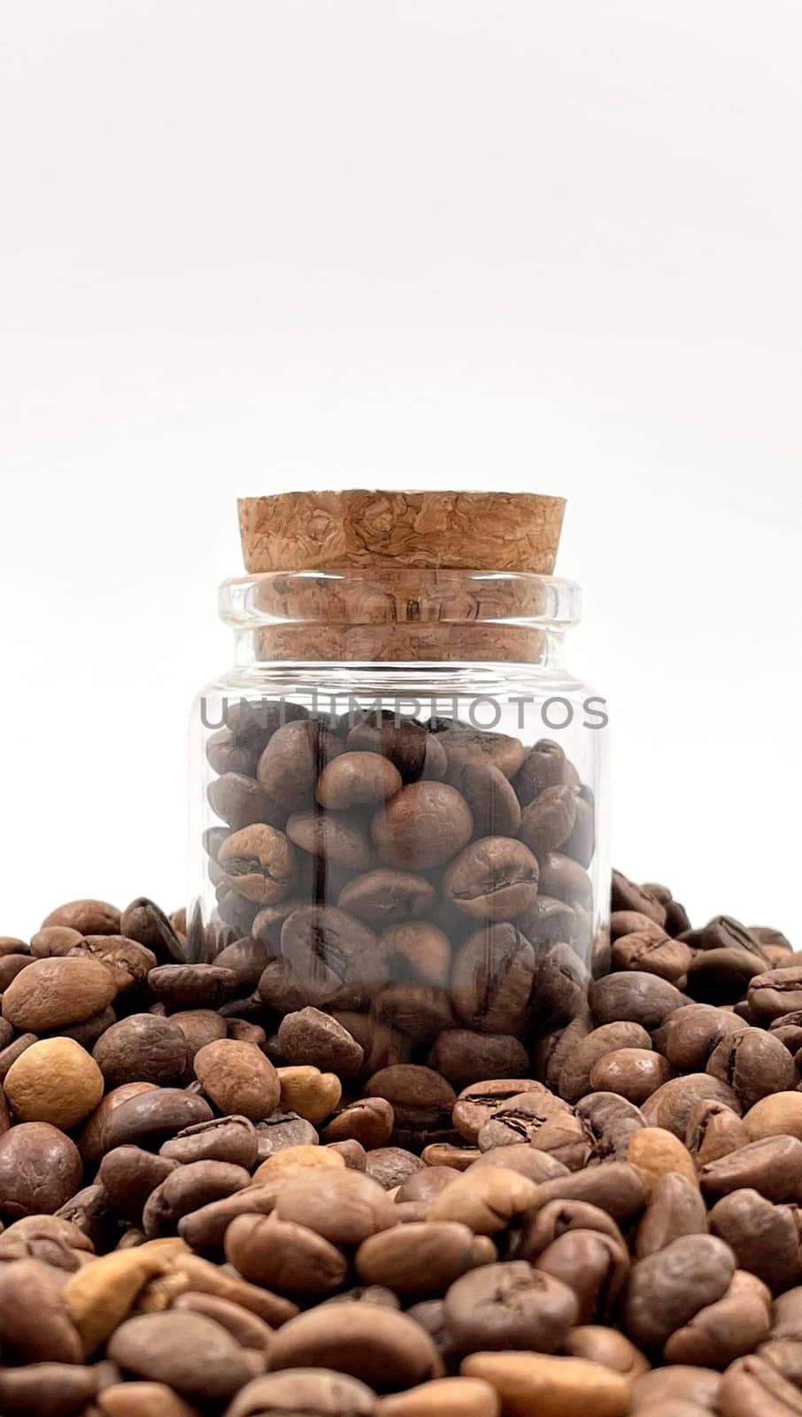 Coffee beans in a small glass jar with a cork lid on the table. Coffee beans packed in a transparent, airtight storage container. Coffee seeds inside a glass jar
