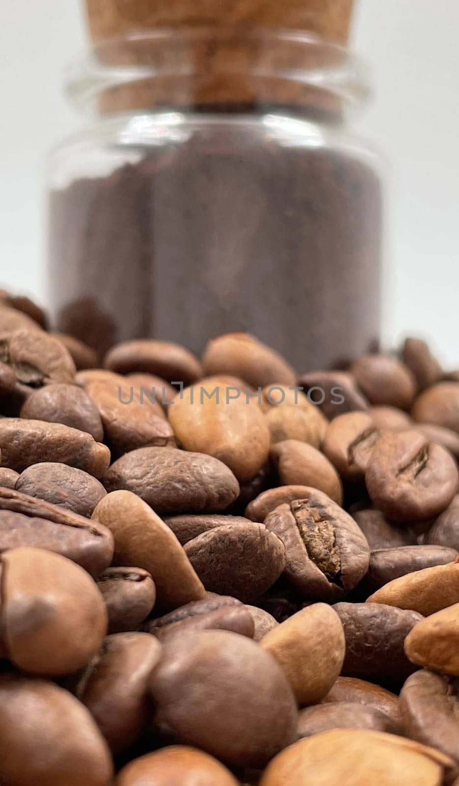Coffee beans ground in a coffee grinder, mortar or mill in a small glass jar on the table. Coarse or medium grind are packed for storage. A drink made from roasted and ground grains
